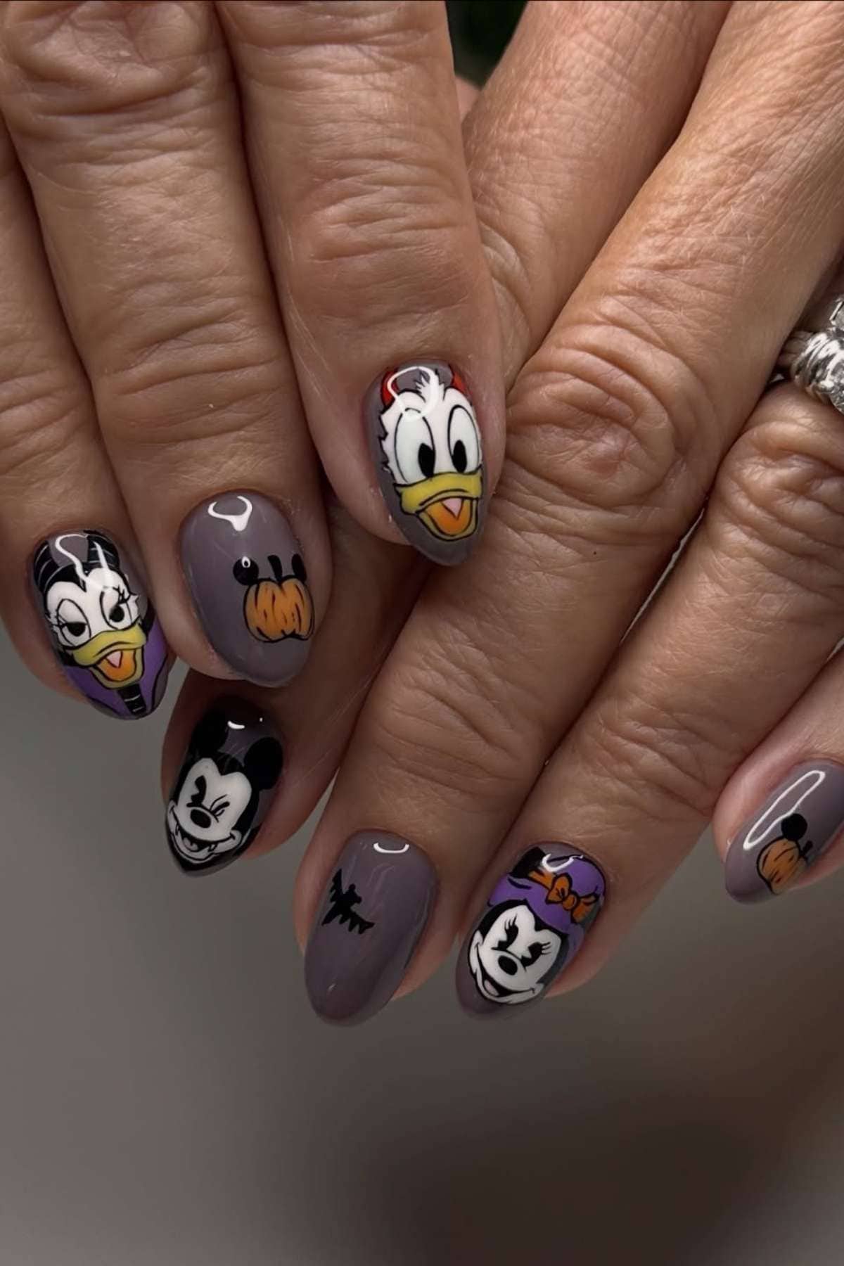 Close-up of hands with manicured nails featuring cartoon characters including Donald Duck, Daisy Duck, Mickey Mouse, and Minnie Mouse on a gray base.