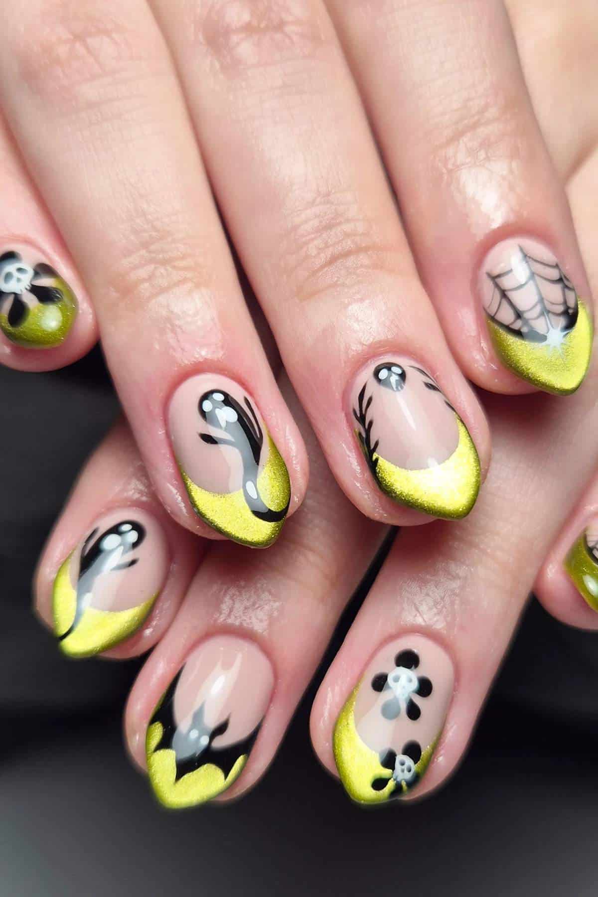 Hands with manicured nails featuring neon yellow French tips, black and white ghost, spiderweb, and flower designs on a nude background.