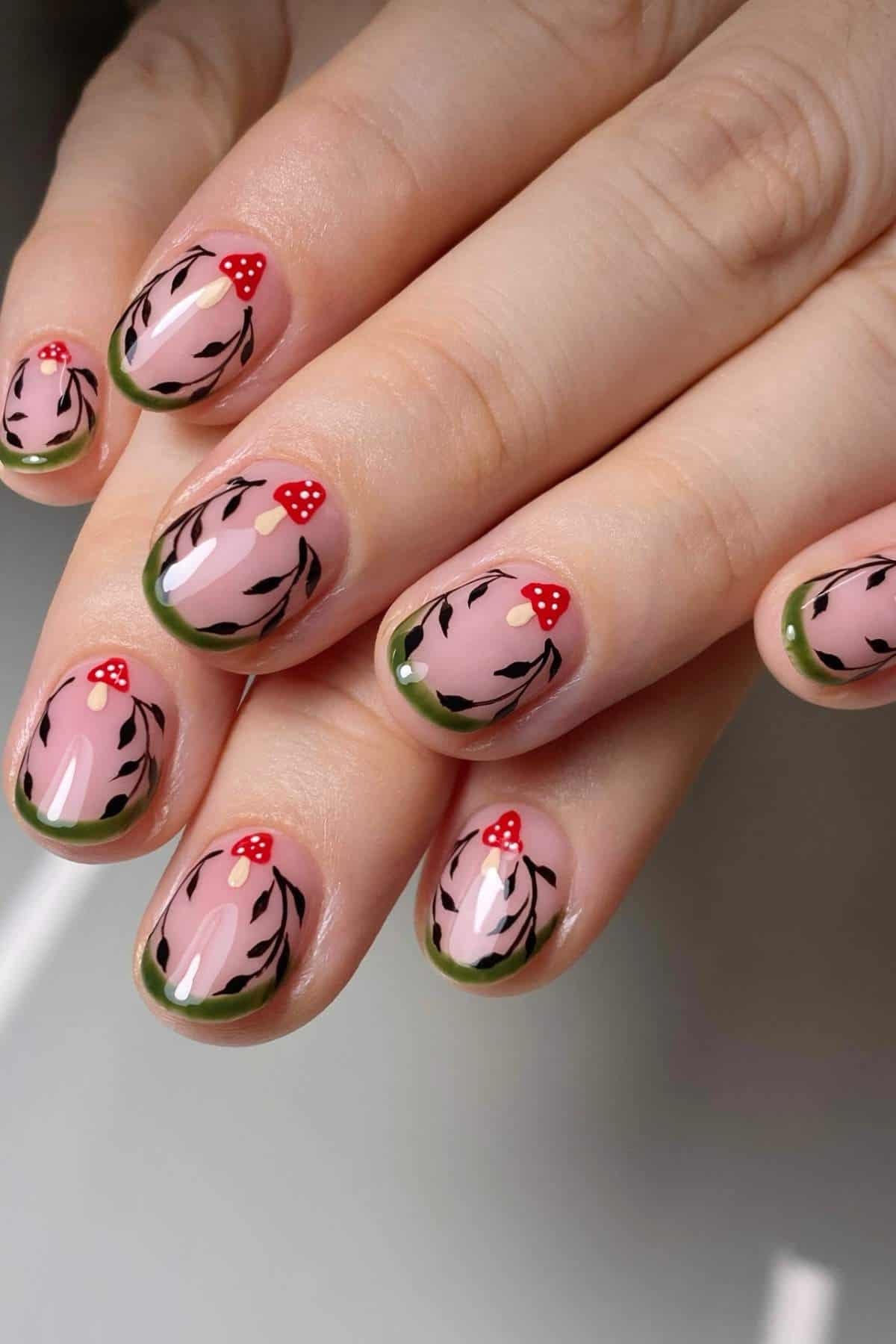 Fingernails with pink base, green French tips, black leaf designs, and small red mushrooms with white spots painted on each nail.