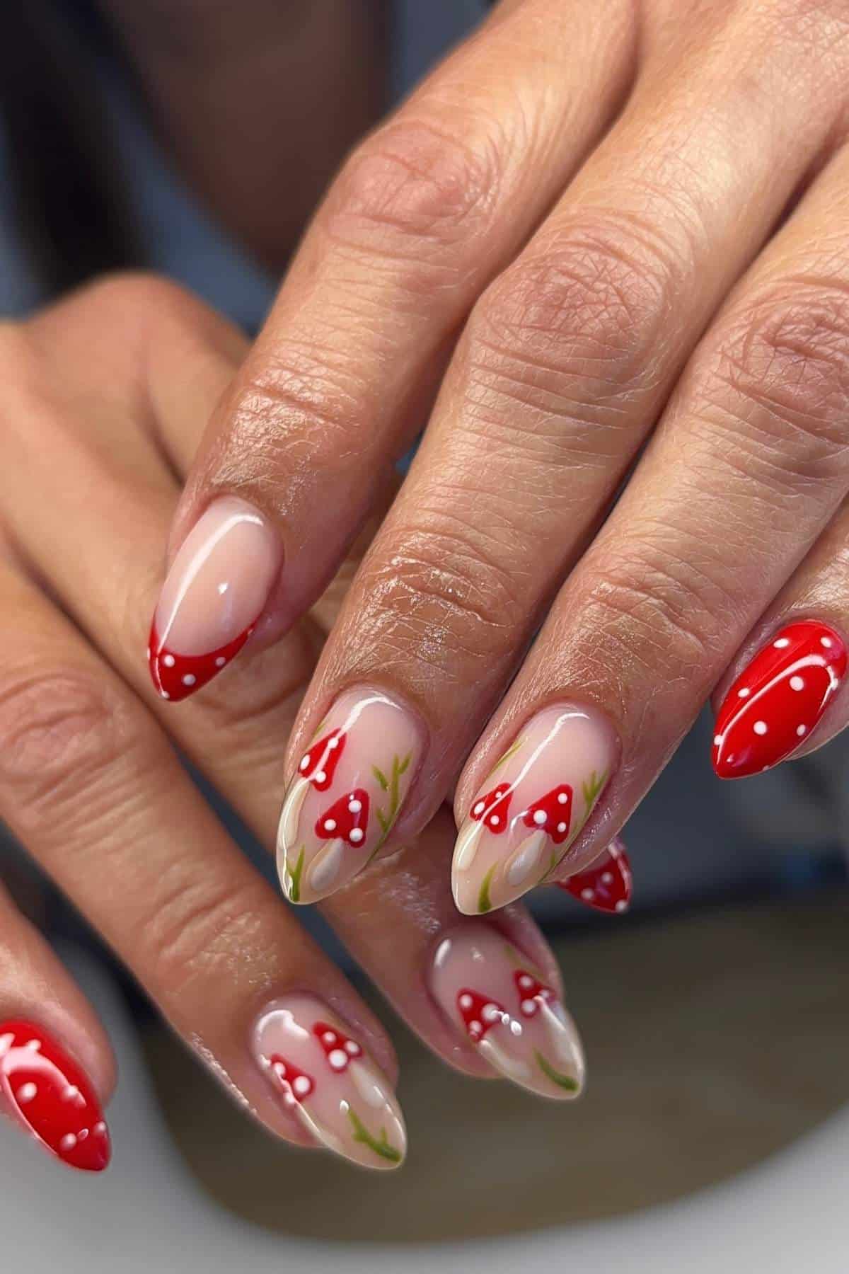 Hands with almond-shaped nails featuring red and white mushroom designs with green stems on a nude base.
