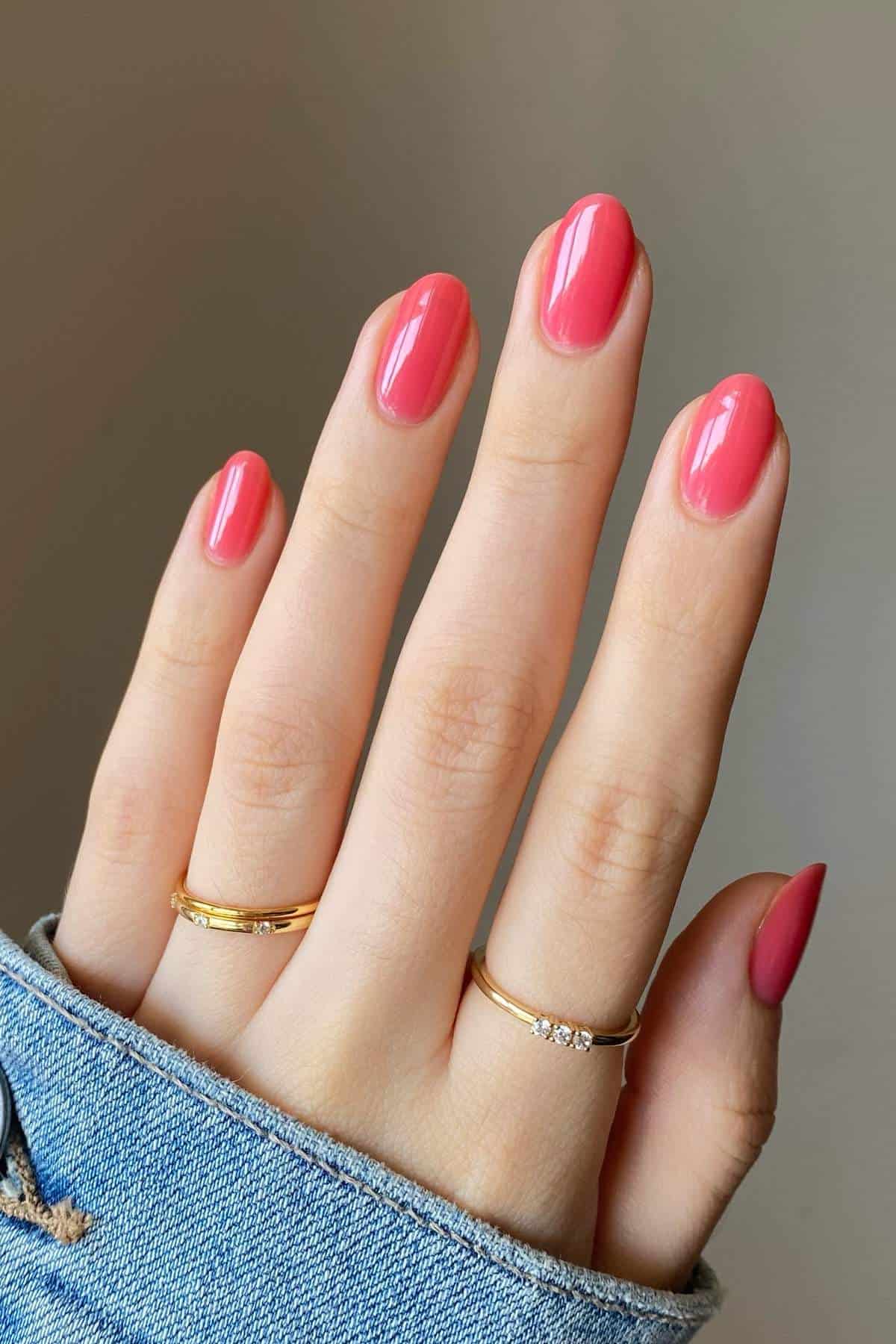 A hand with neatly manicured pink nails, wearing two simple gold rings, is shown against a neutral background. The person is wearing a blue denim sleeve.