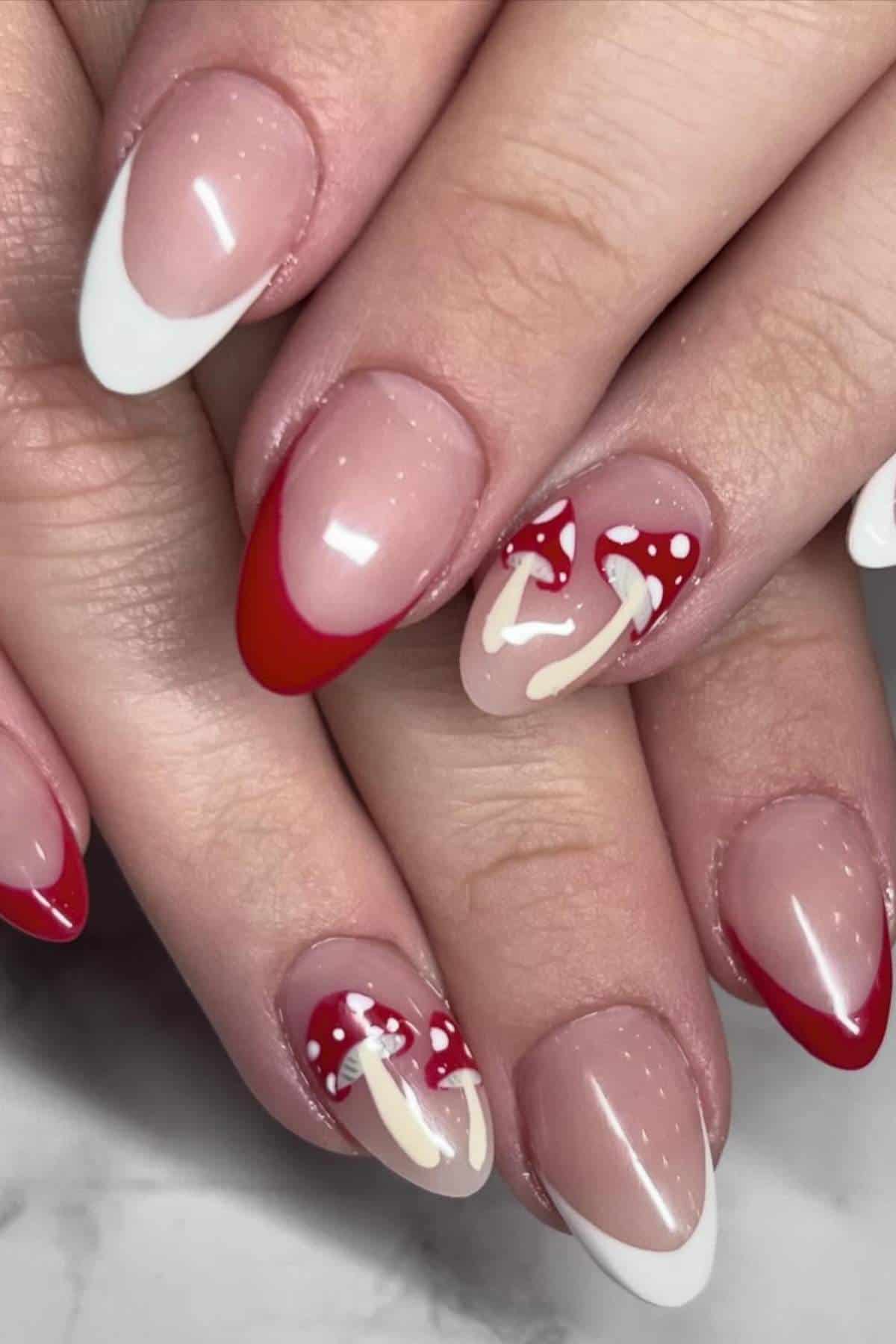 Close-up of hands with manicured nails featuring red and white French tips and two accent nails with painted red and white mushroom designs.
