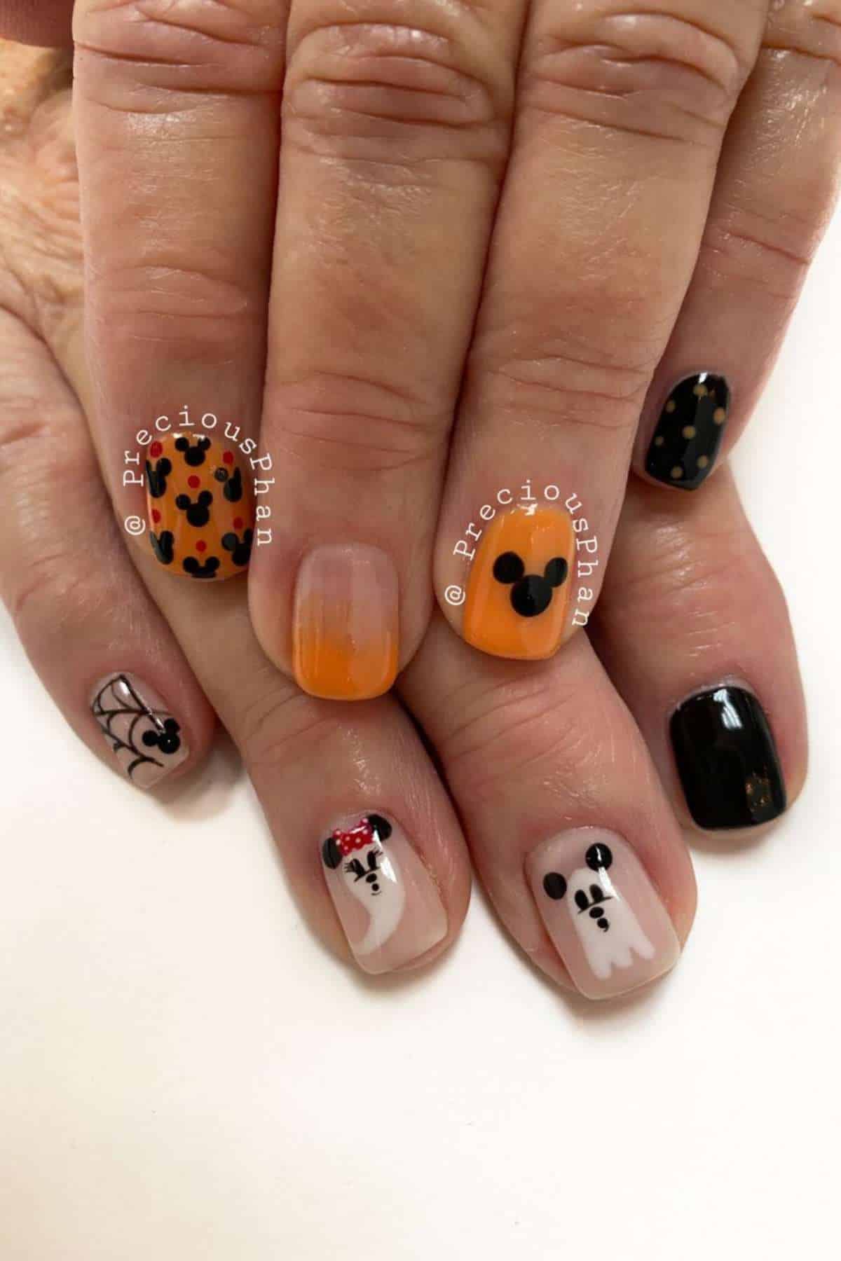 Five fingernails with Halloween-themed designs, including Mickey Mouse heads, spider webs, orange and black polish, and ghost faces.