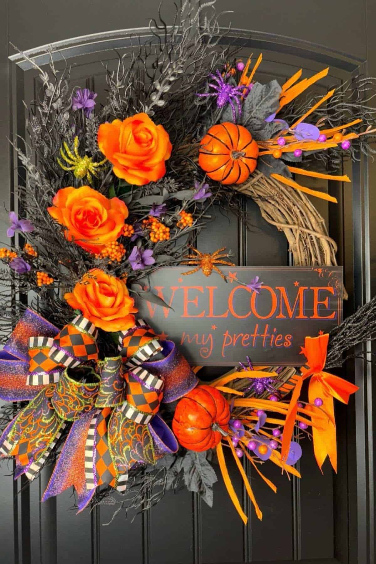 A Halloween wreath with orange roses, mini basketballs, ribbons, and a sign reading "WELCOME my pretties" hangs on a black door.