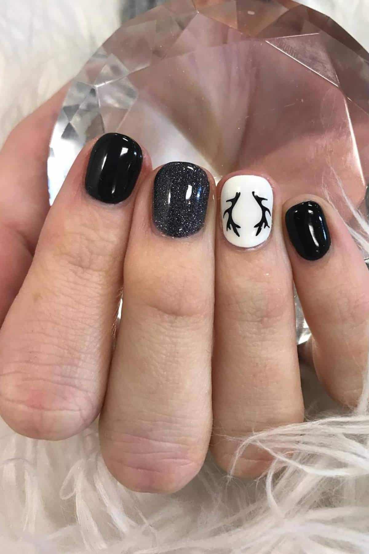 A hand with short nails, four painted black, one white with a simple antler design, holding a faceted crystal.