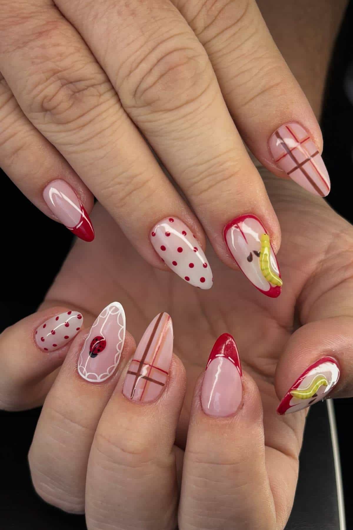 Hands showing manicured nails with red tips, polka dots, stripes, abstract designs, and a small rose on a neutral pink base.