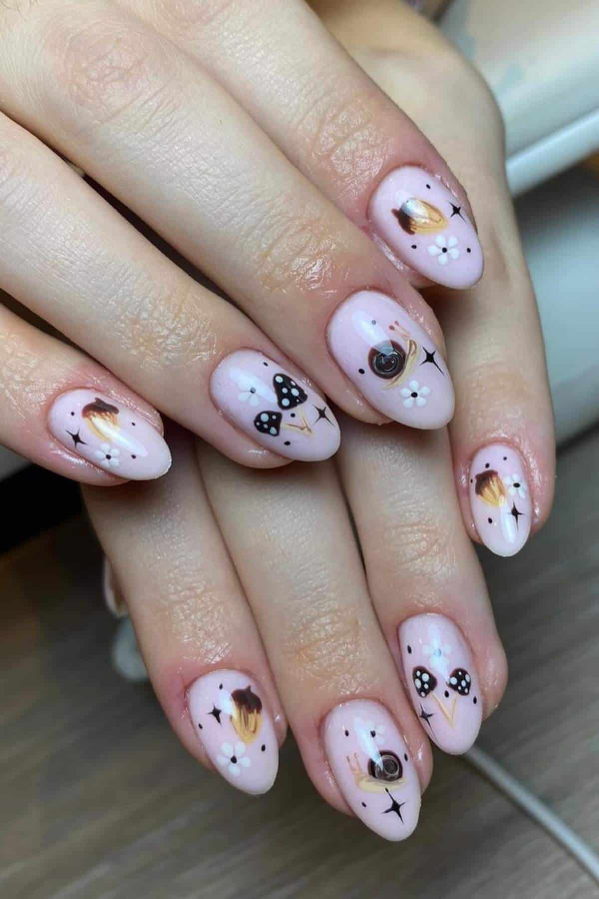 Hands with almond-shaped nails featuring nude polish and black-and-white mushroom and snail designs, along with small abstract patterns and dots.