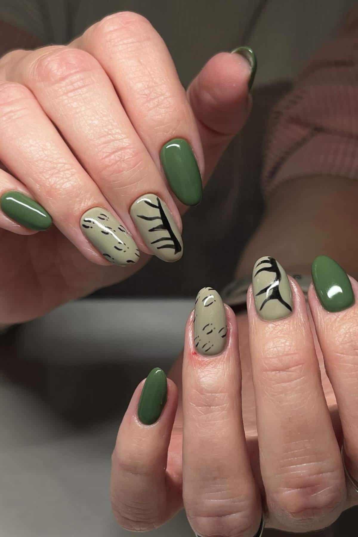 Hands with almond-shaped nails, painted in dark green and beige with black abstract lines and dots as nail art.