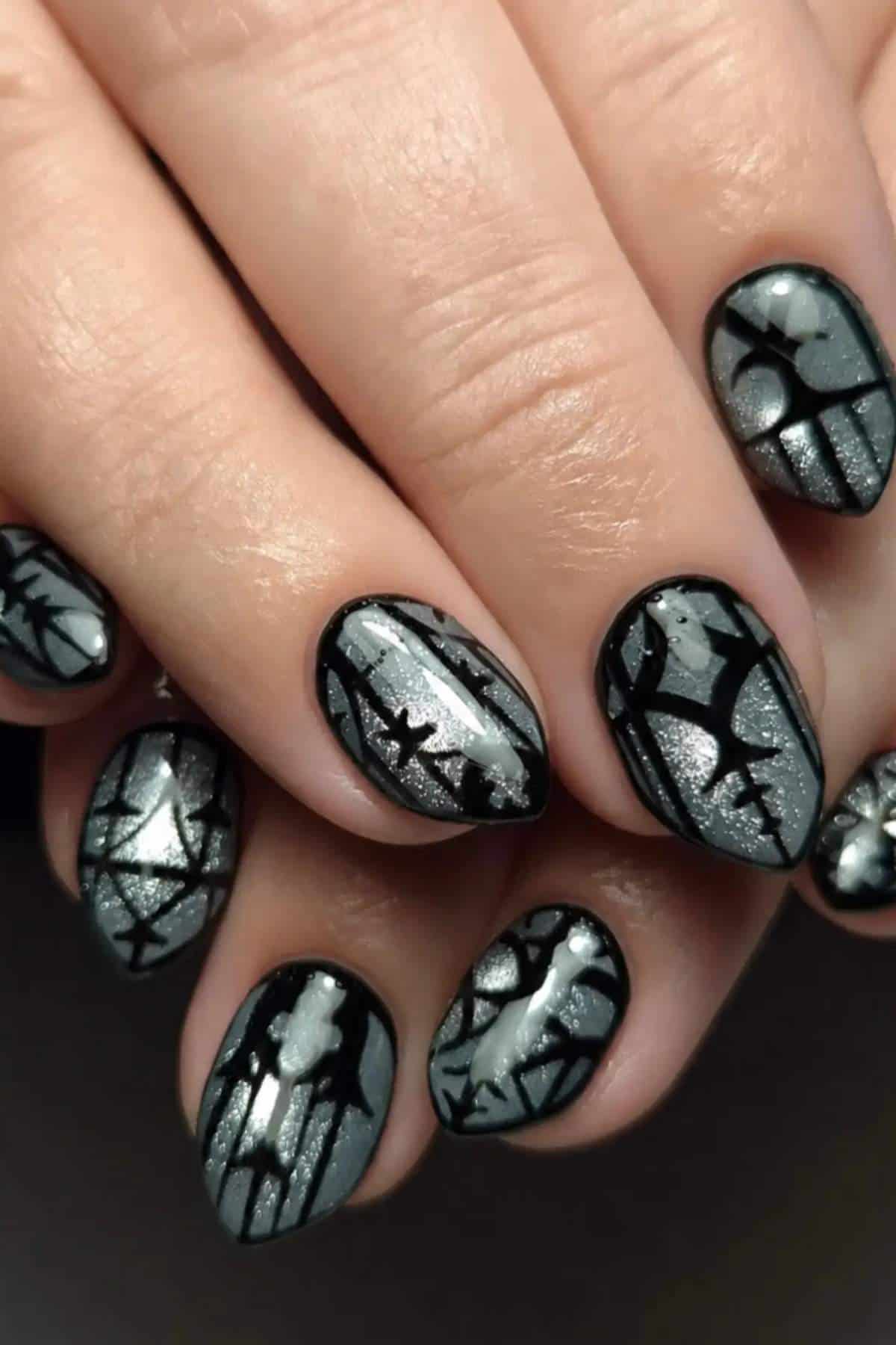 Close-up of fingernails with a silver and black spiderweb and bat nail art design, featuring shiny accents and matte background.