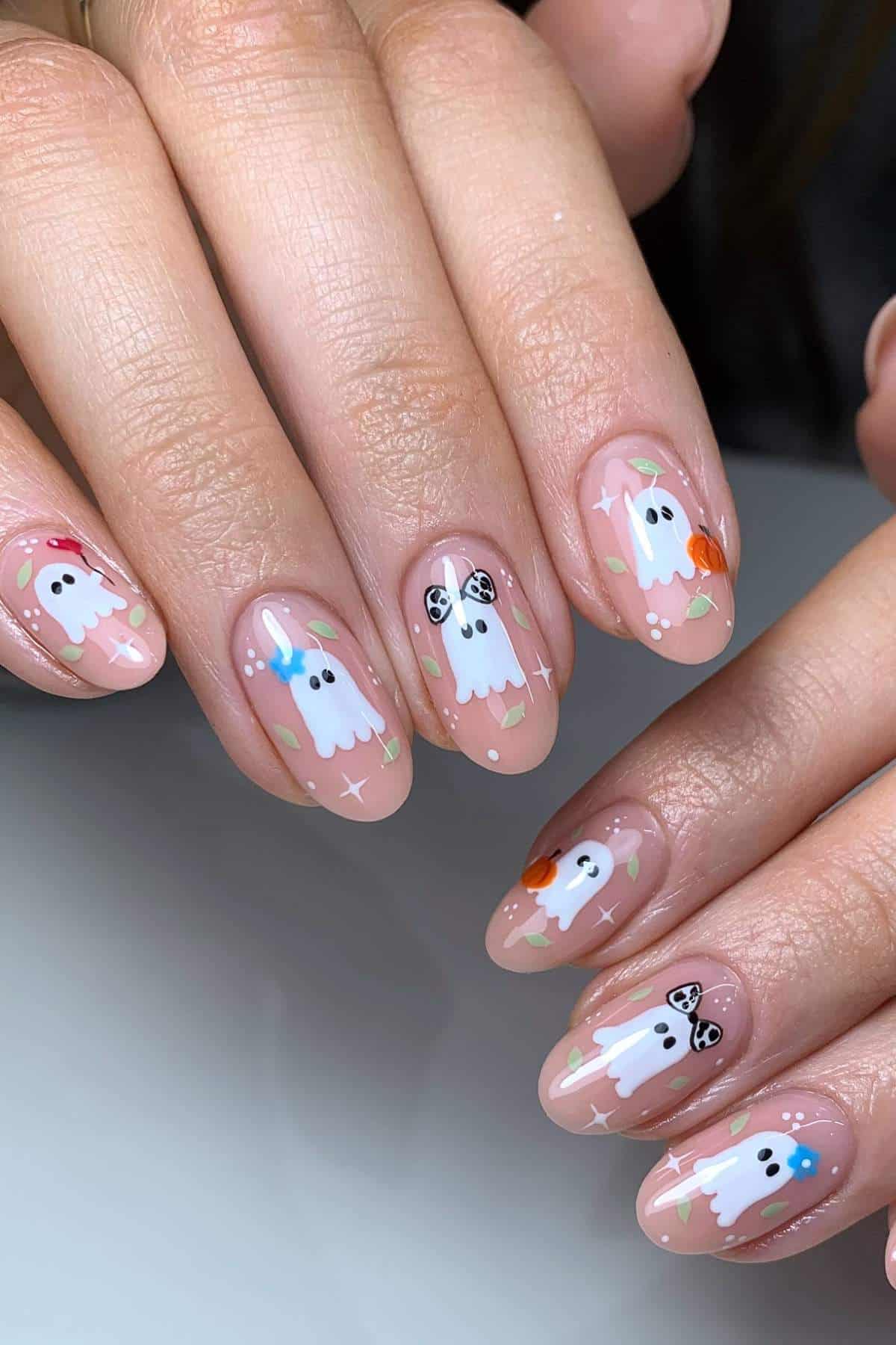 Close-up of hands with nude nail polish featuring white ghost designs, colorful stars, butterflies, and small autumn-themed decorations.