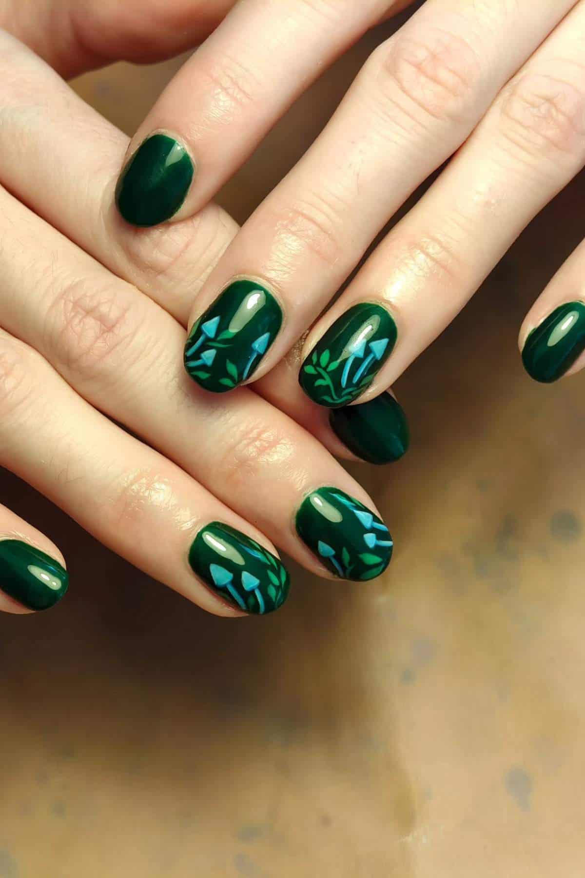 Hands with oval-shaped nails painted dark green; some nails feature blue and green geometric leaf designs.