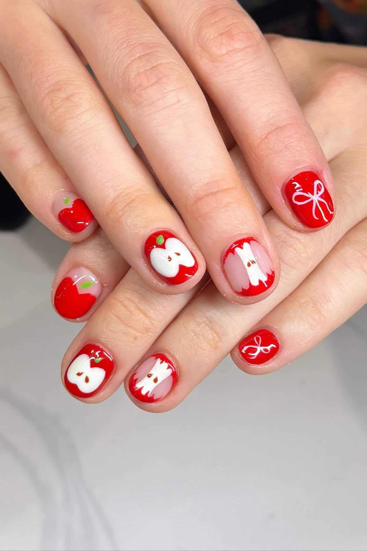 Fingernails painted red with white apple and bow designs on each nail.
