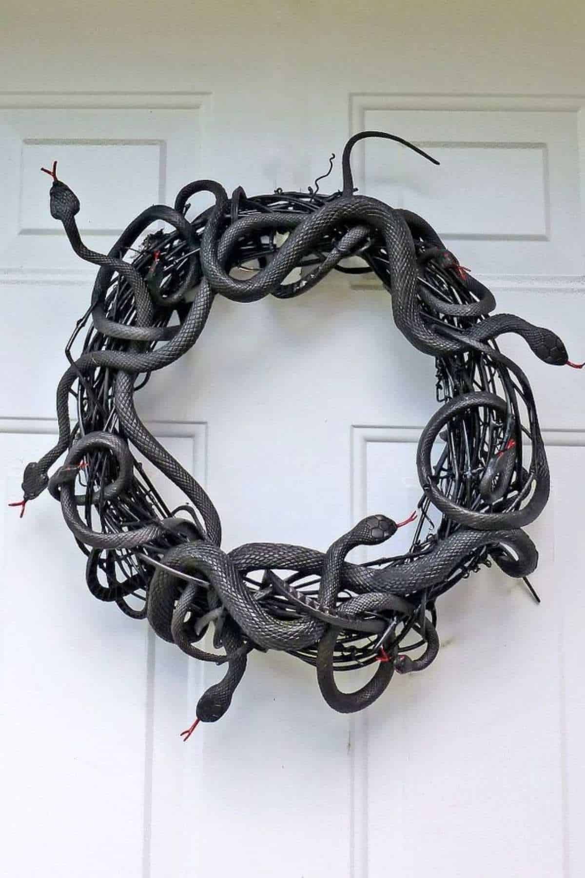 A wreath made of intertwined black fake snakes with red tongues is hanging on a white door.