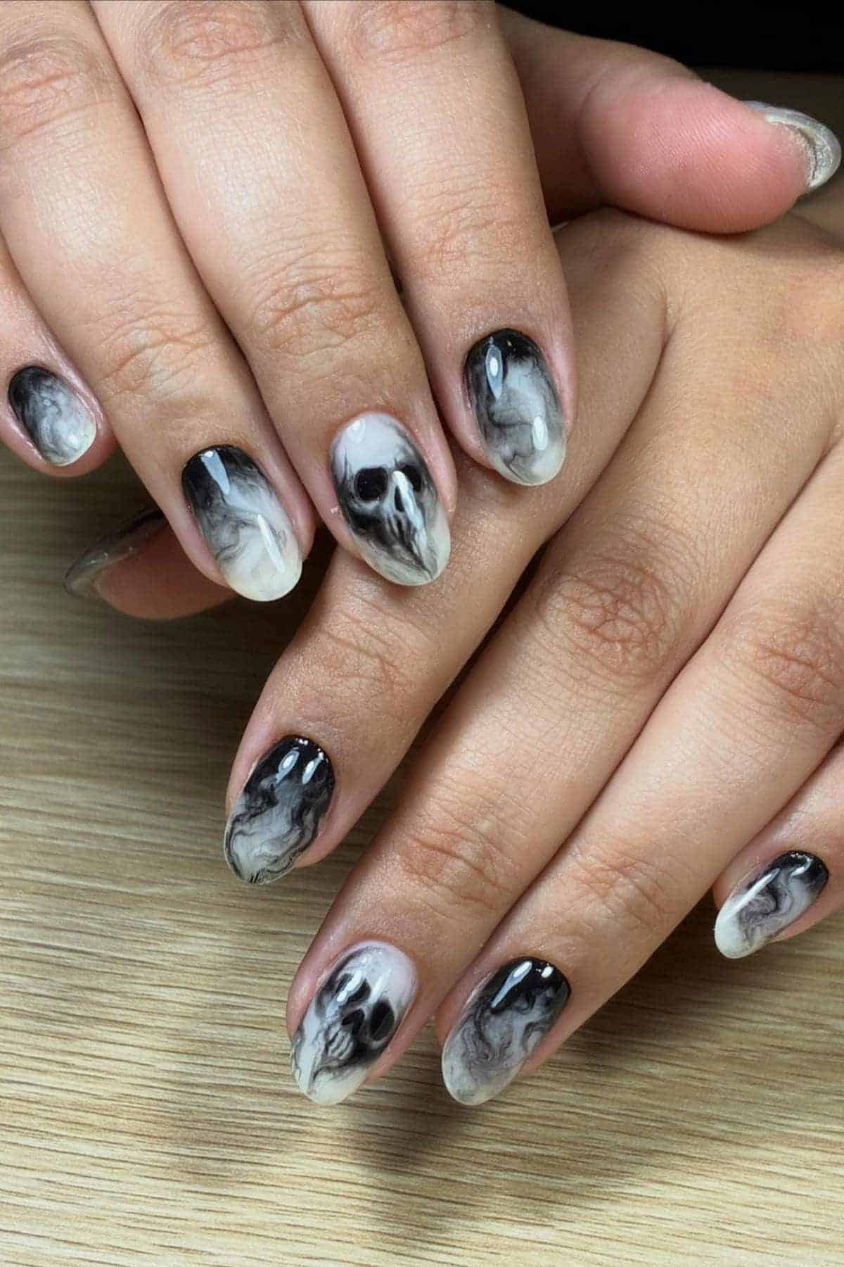 Hands with short, oval-shaped nails featuring a black and white marbled design, displayed on a light wooden surface.
