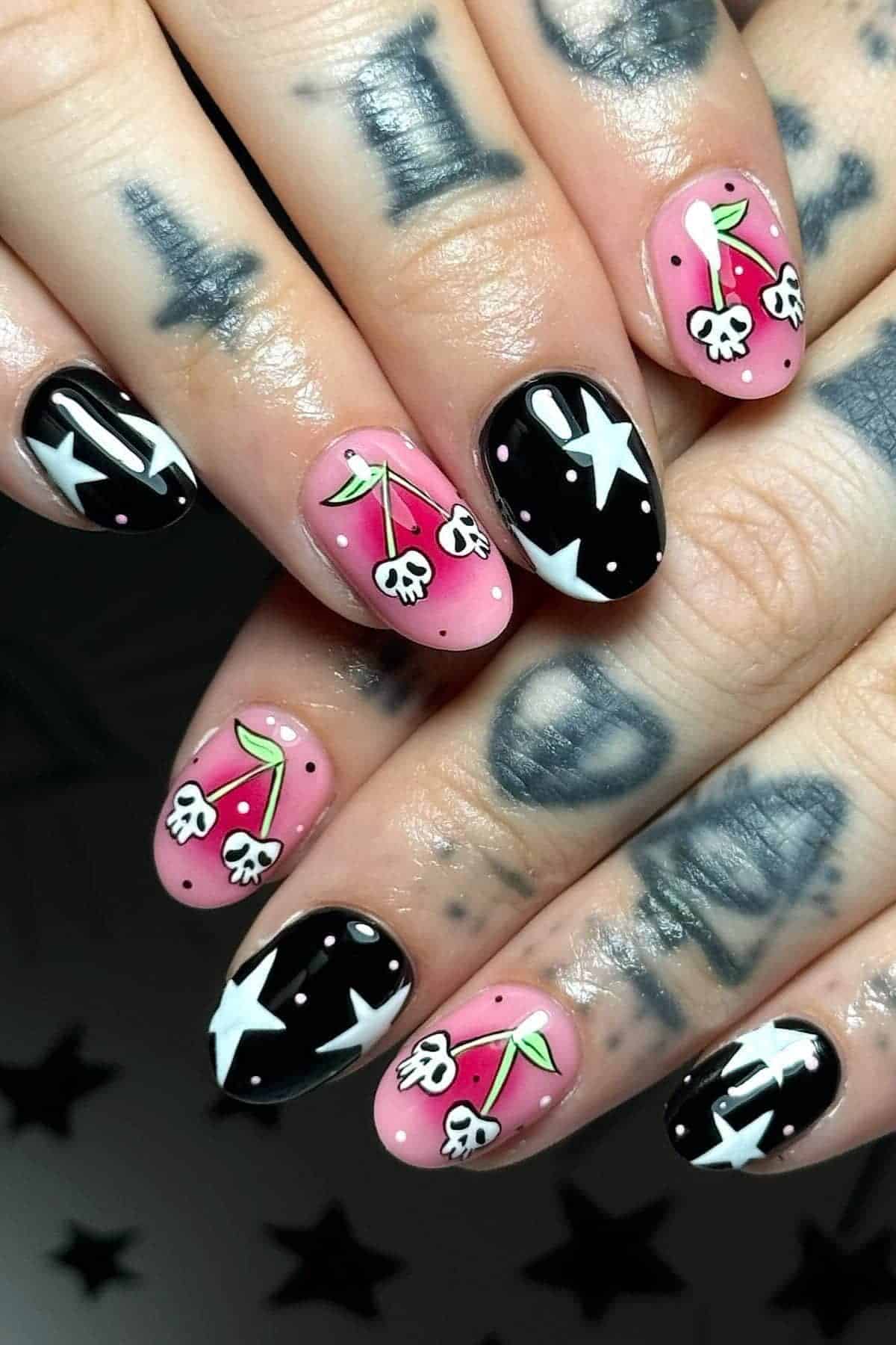 Close-up of hands with tattoos, featuring nails painted with alternating pink and black polish, decorated with white stars and cherry designs.
