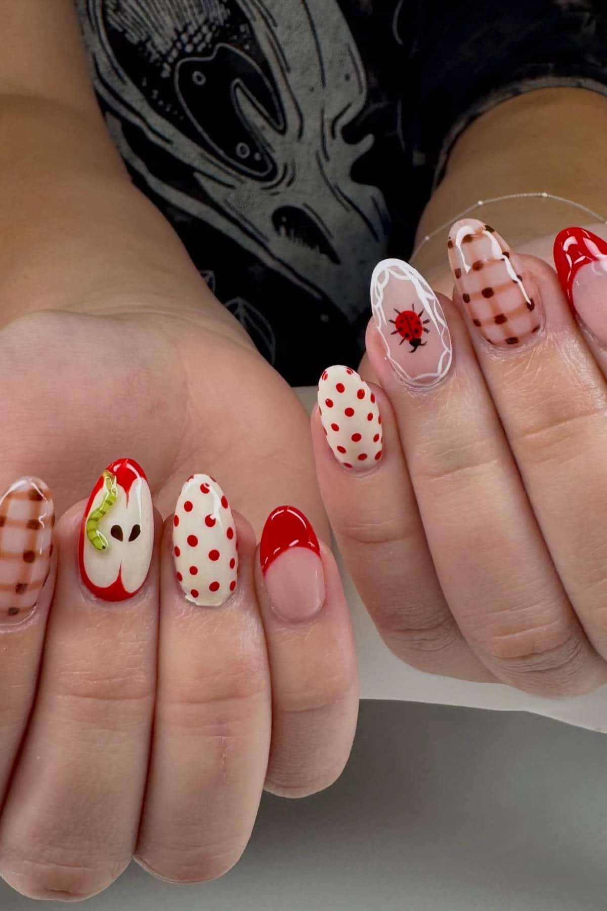 Hands with long nails featuring various nail art designs, including red French tips, polka dots, plaid, a red bug, and an apple slice design.