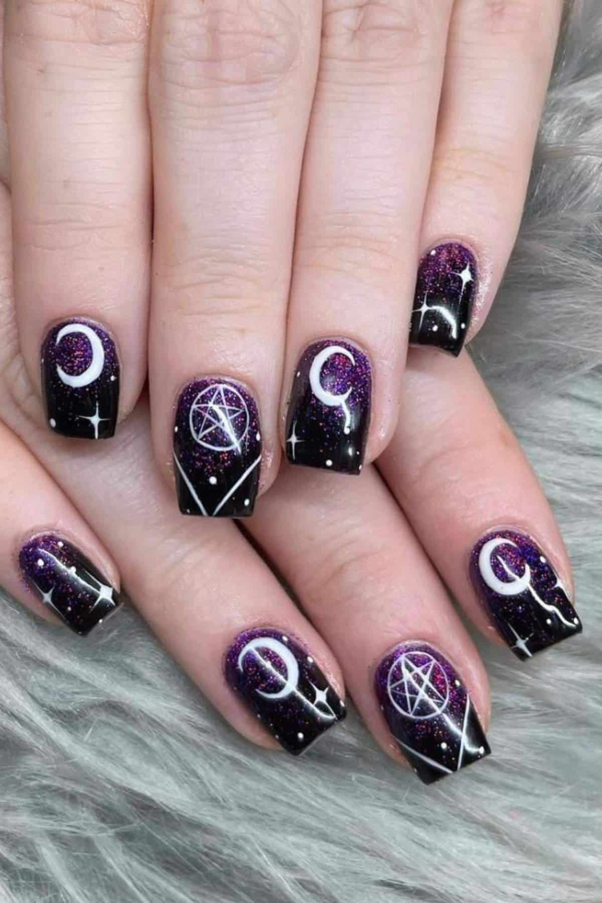 Fingernails painted with a dark purple galaxy theme, decorated with moons, pentagrams, and white star designs.