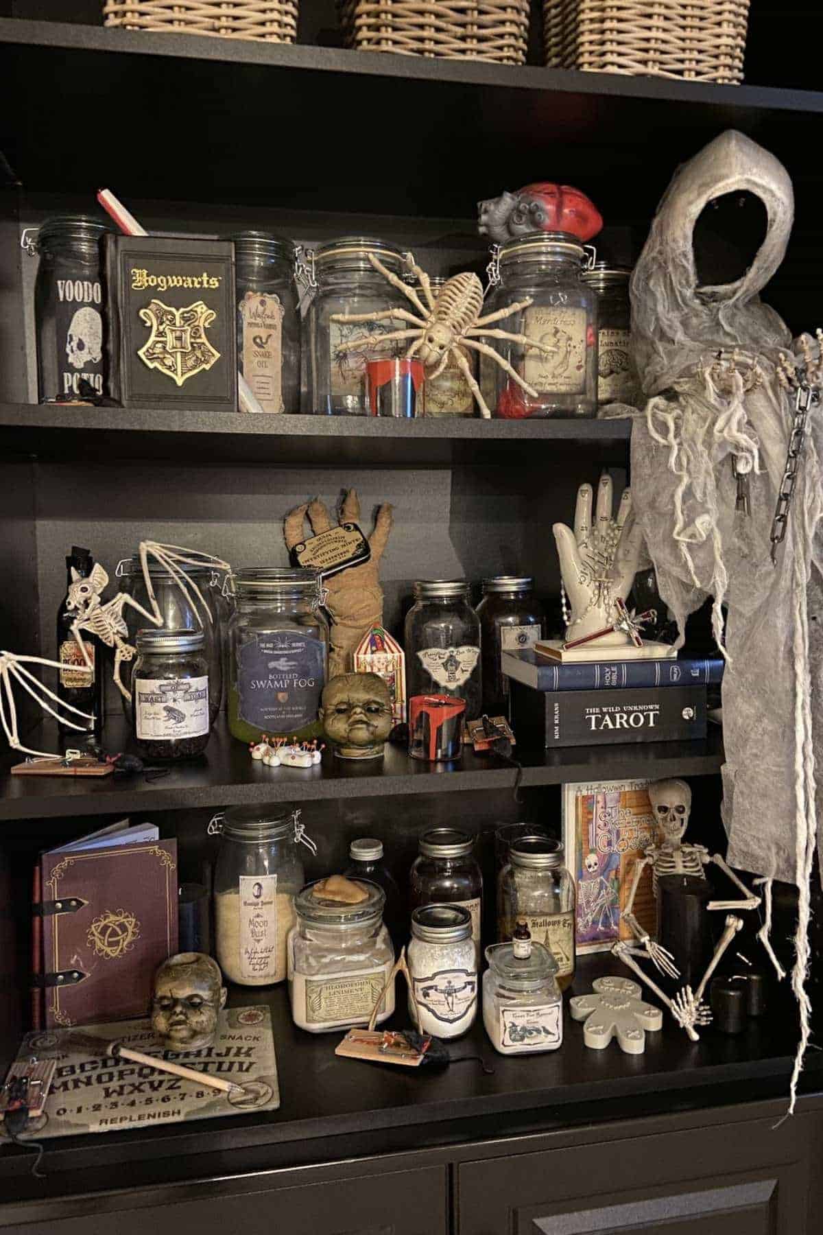 Shelves filled with jars, skulls, tarot cards, a skeleton, spell books, and a gray hooded figure, arranged as eerie, occult-themed decorations.