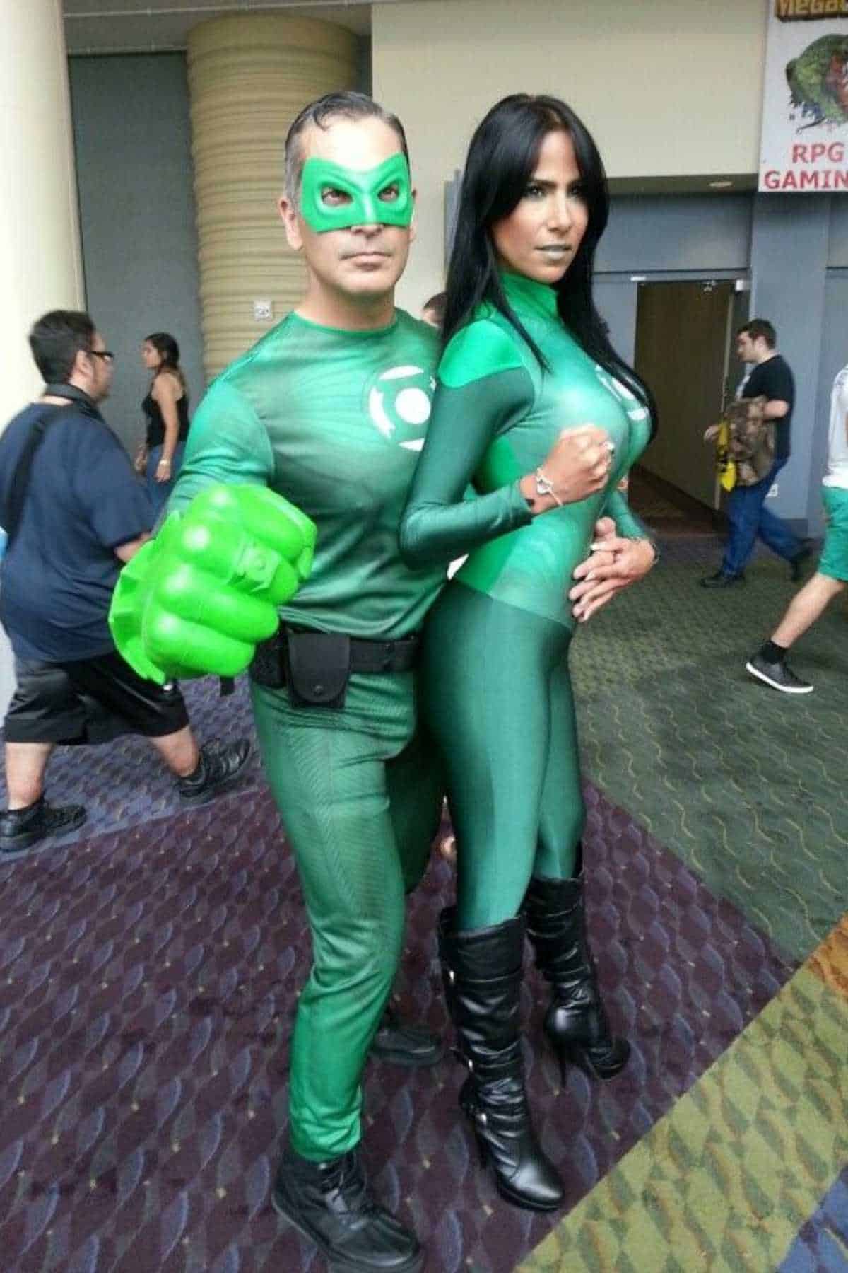 Two people dressed in Green Lantern superhero costumes pose together at a convention. The man wears a mask and foam fist; the woman has long black hair and knee-high boots.