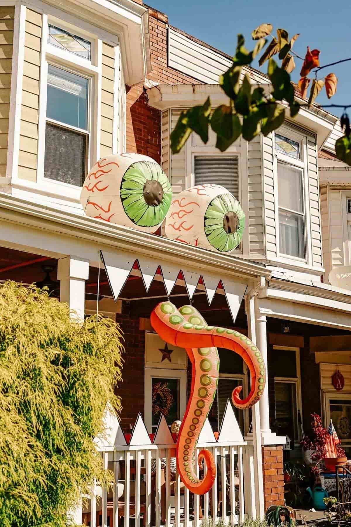 A house decorated with large inflatable eyes, white triangular teeth, and an inflatable orange tentacle emerging from the porch.