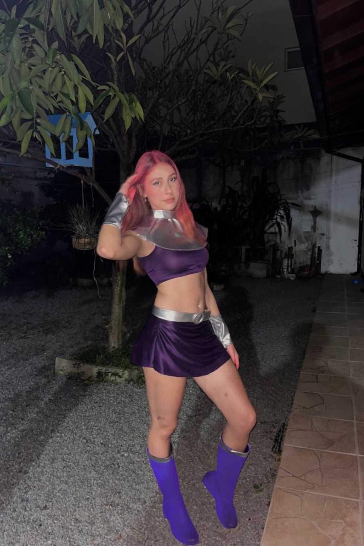 Person wearing a purple and silver superhero costume with long pink hair standing outdoors at night on a gravel surface.