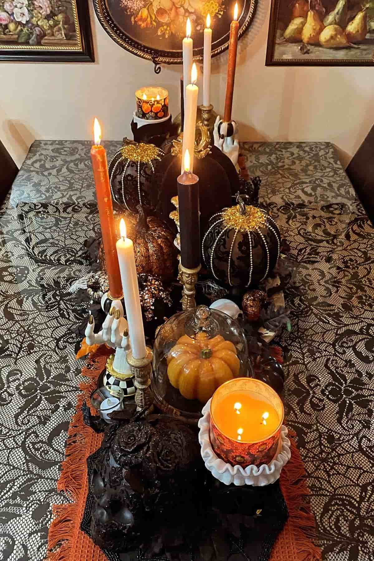 A decorated table with lit candles, ornamental pumpkins, and lace tablecloth, set for a festive autumn or Halloween gathering.