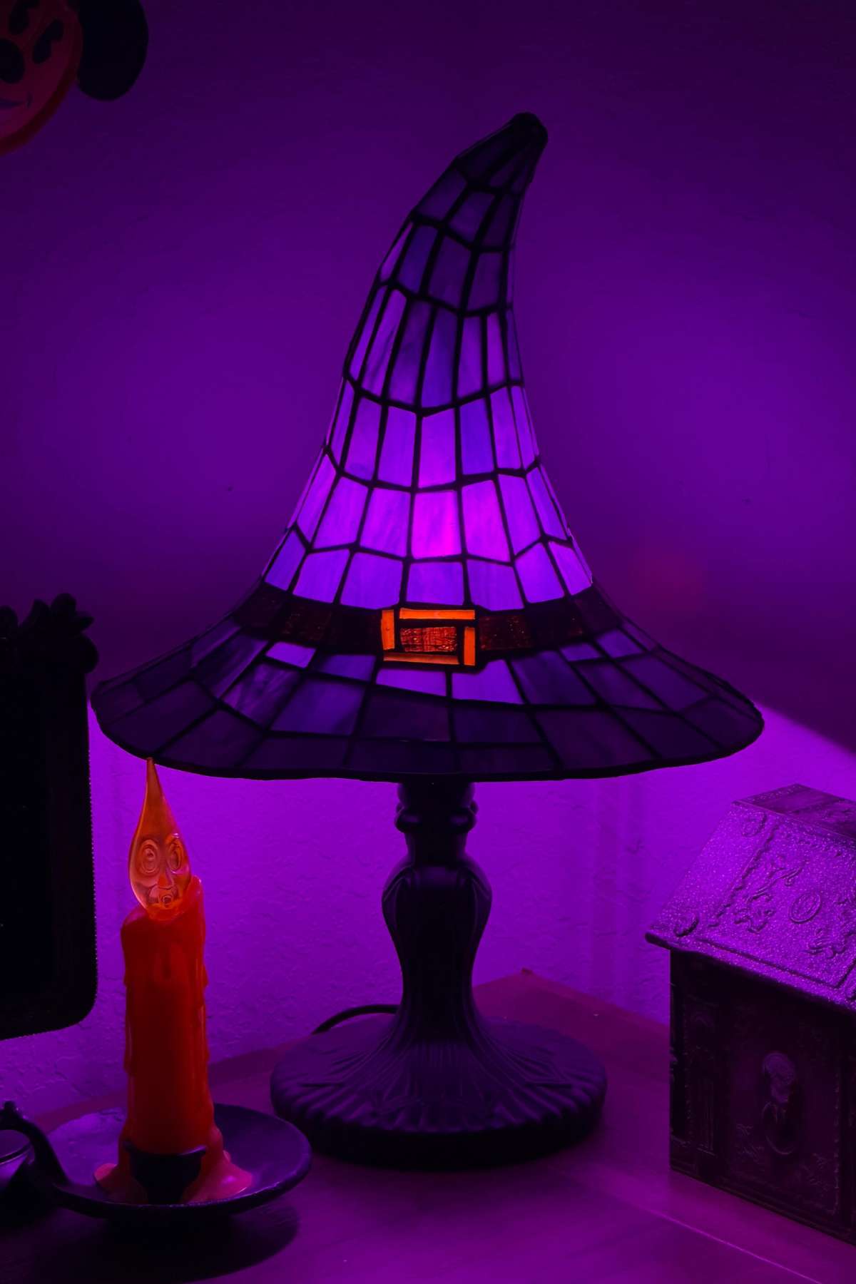 A purple witch hat lamp glows on a table next to an orange candle shaped like a face and a small decorative house.