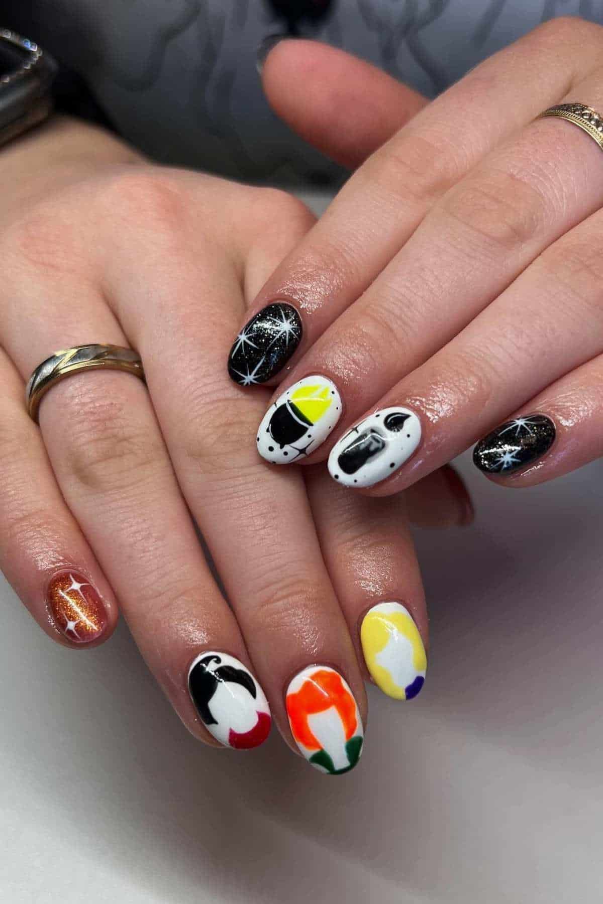 Hands with painted nails featuring colorful abstract designs, black with white star patterns, a brown metallic accent, and a watch and rings on the fingers.