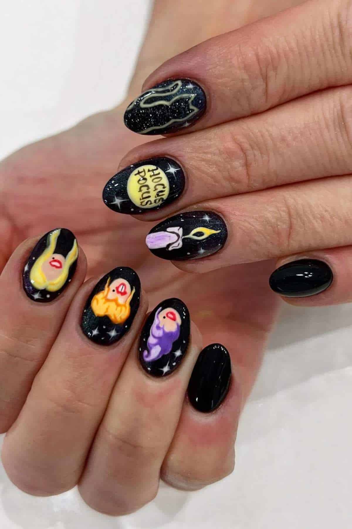 Hands with black nail polish featuring colorful, detailed designs inspired by the movie “Hocus Pocus,” including faces, a spell book, and stars, on medium-length oval nails.