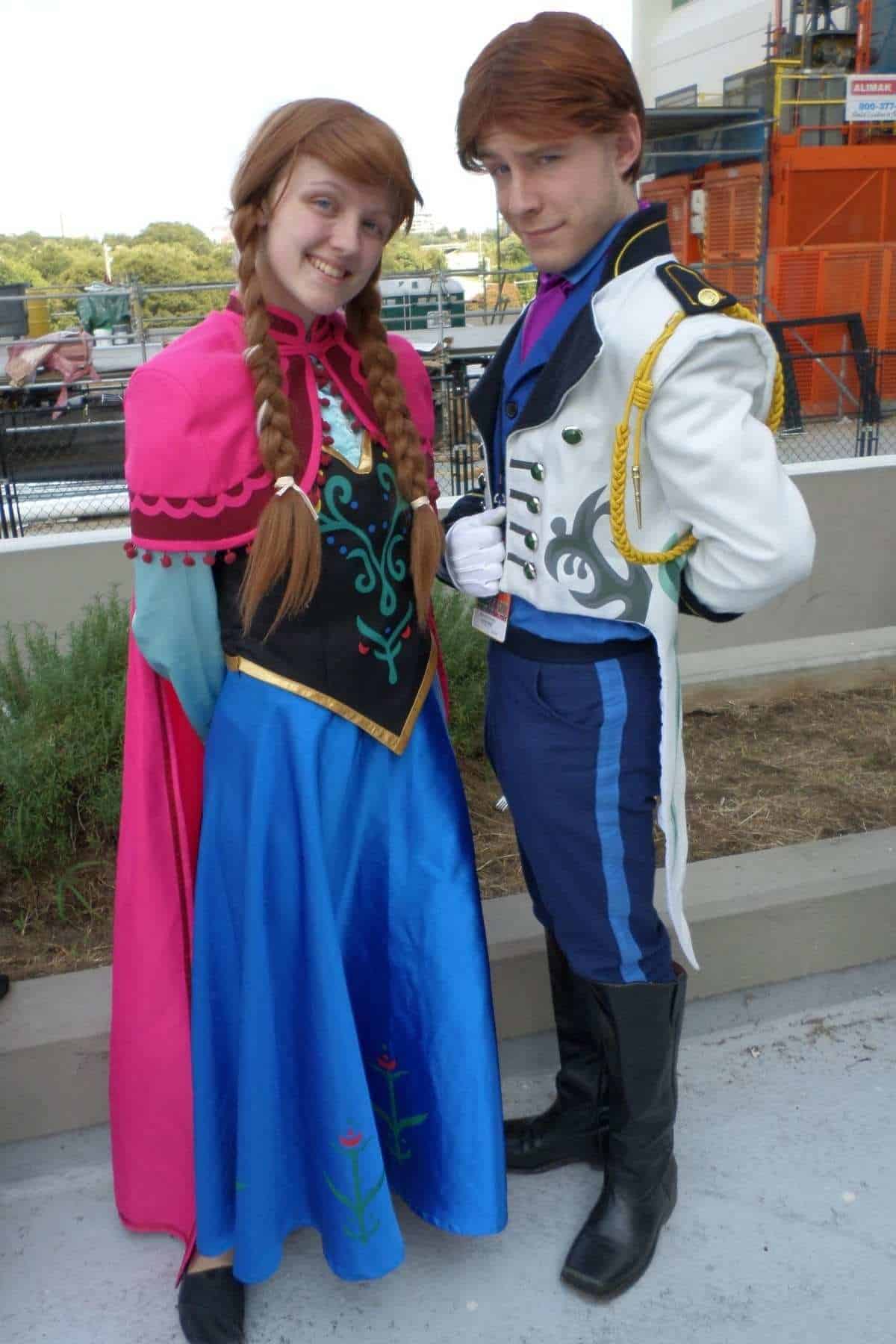 Two people dressed in costumes as Anna and Hans from Frozen stand side by side outdoors, smiling at the camera.