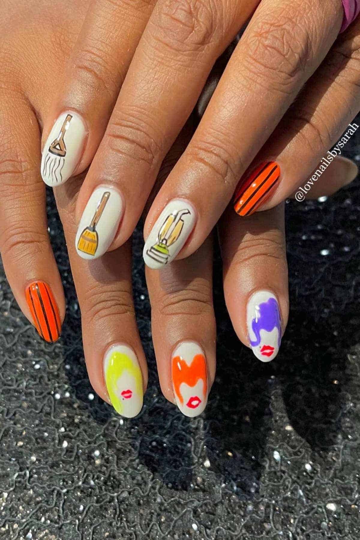 Hands with nail art featuring brushes and makeup items on some nails, abstract colorful faces with lips on others, and red-black vertical stripes on one nail per hand.