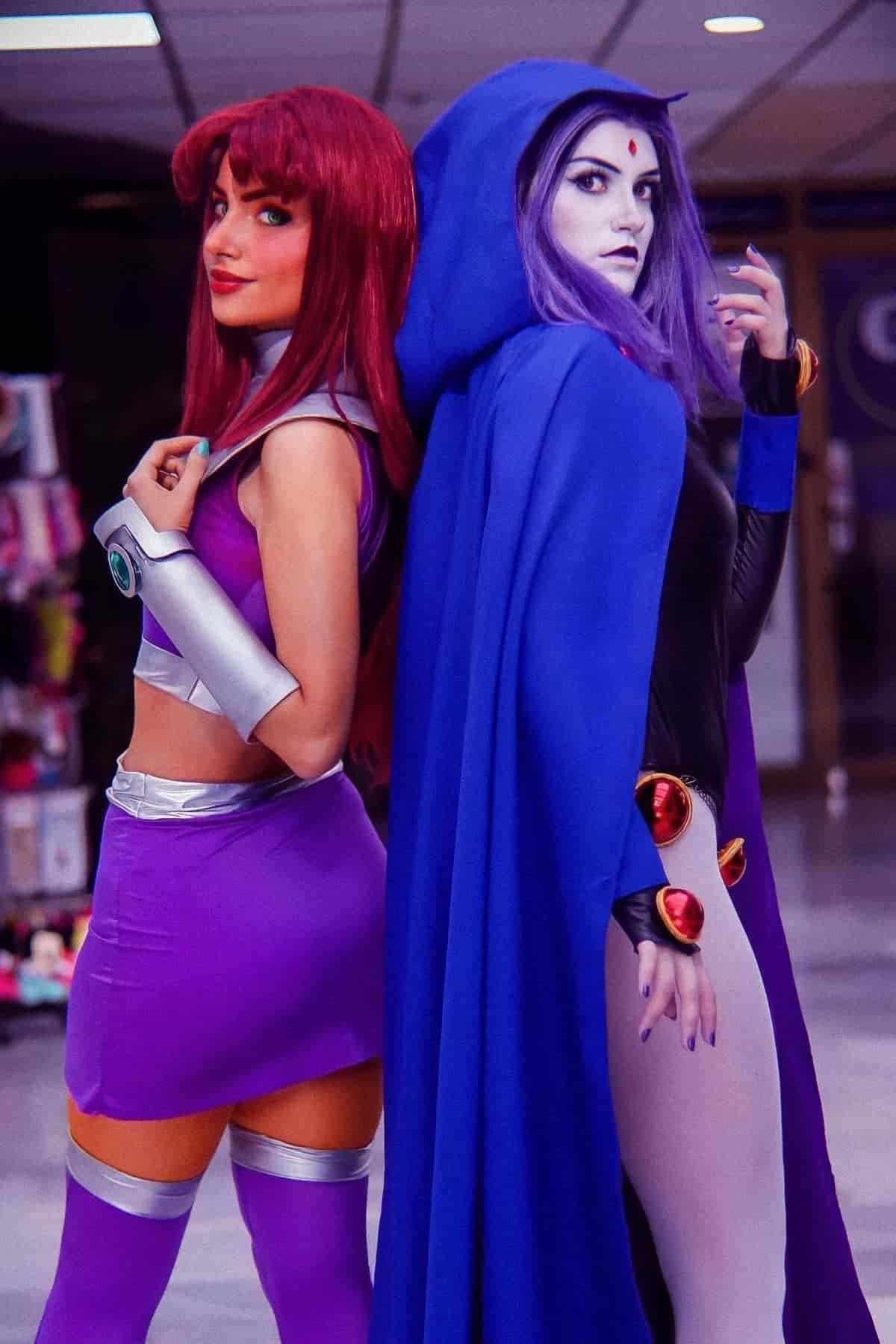 Two people in detailed Starfire and Raven costumes from Teen Titans stand back-to-back indoors, posing for a photo.