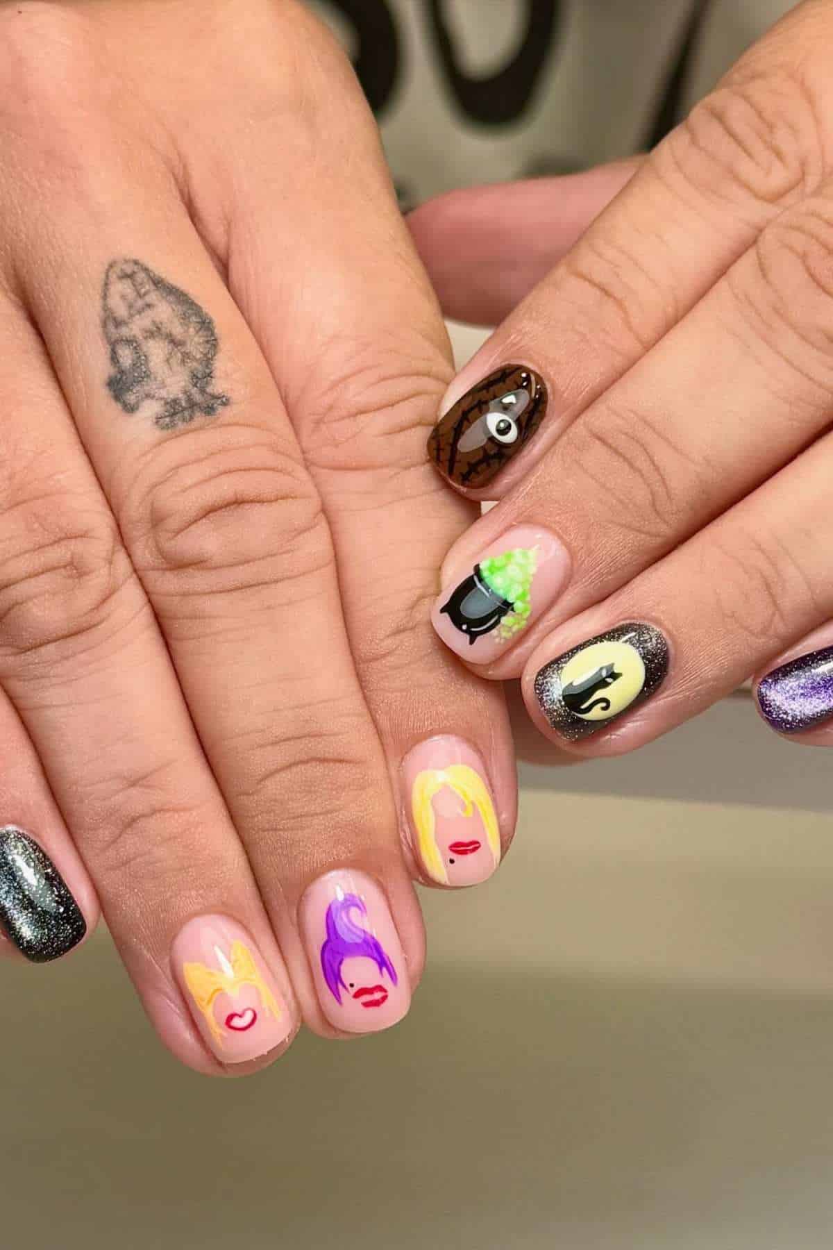 Hands with colorful nail art featuring cartoon faces, a spider web, a black cat, and a cosmic glitter nail; one finger has a black animal tattoo.