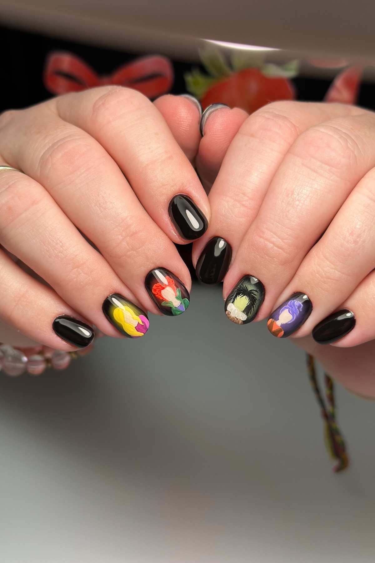 Hands with black-painted nails featuring colorful floral designs on select fingernails.