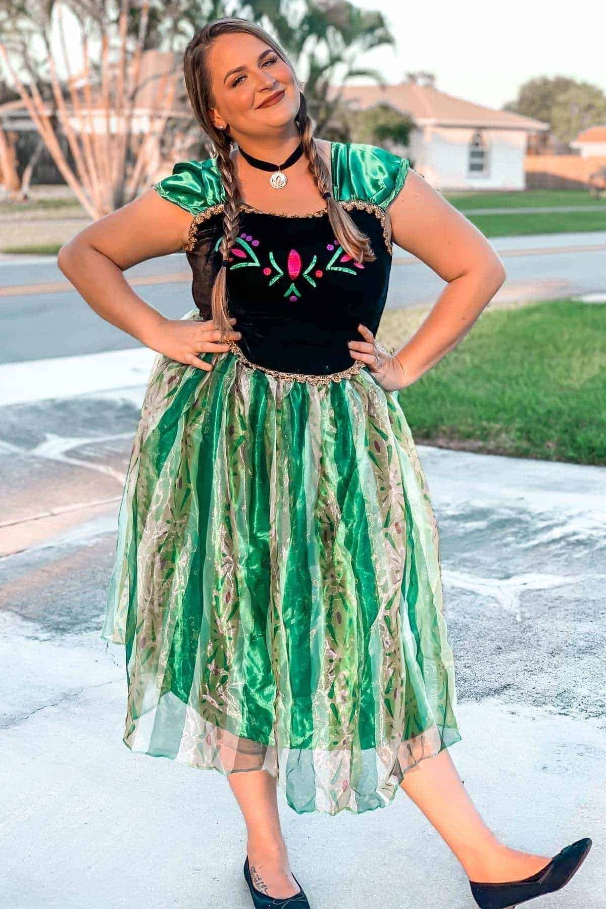 Woman standing outdoors wearing a green and black dress with floral patterns, smiling and posing with hands on hips.