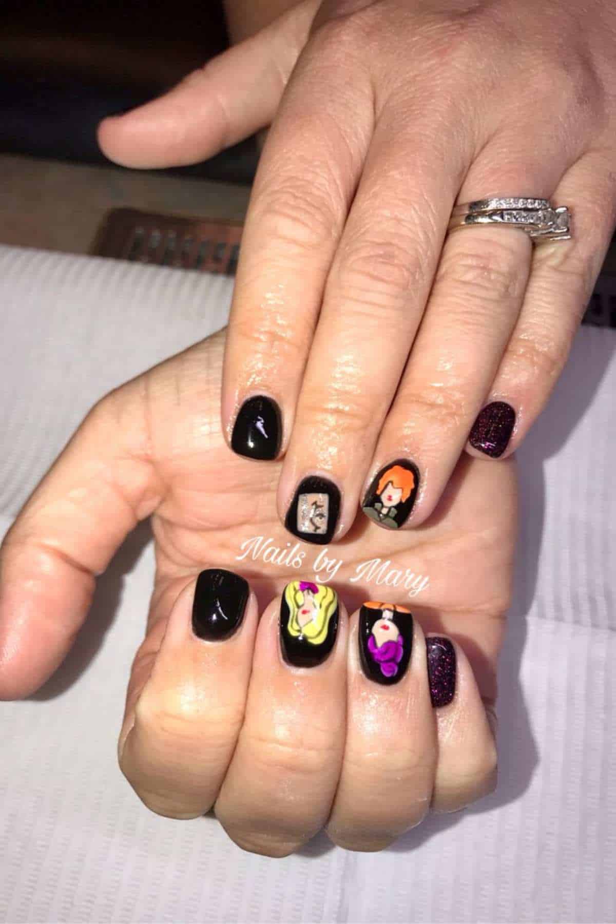 A hand with black nail polish and colorful villain character designs on several nails. The person is wearing a diamond ring. Text on the hand reads “Nails by Mary.”.