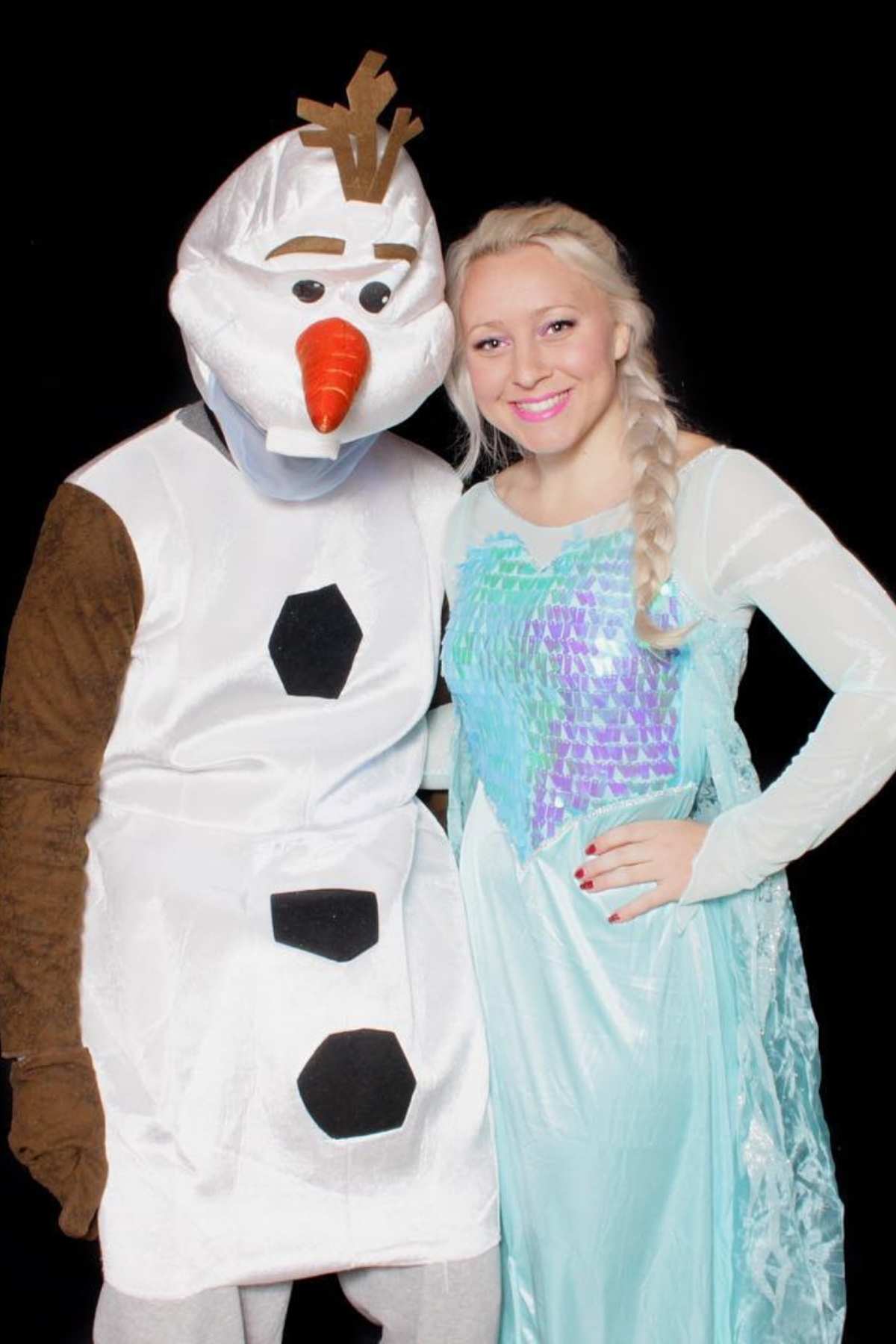 Two people pose in costumes against a black background; one is dressed as Olaf the snowman and the other as Elsa, both characters from the movie Frozen.