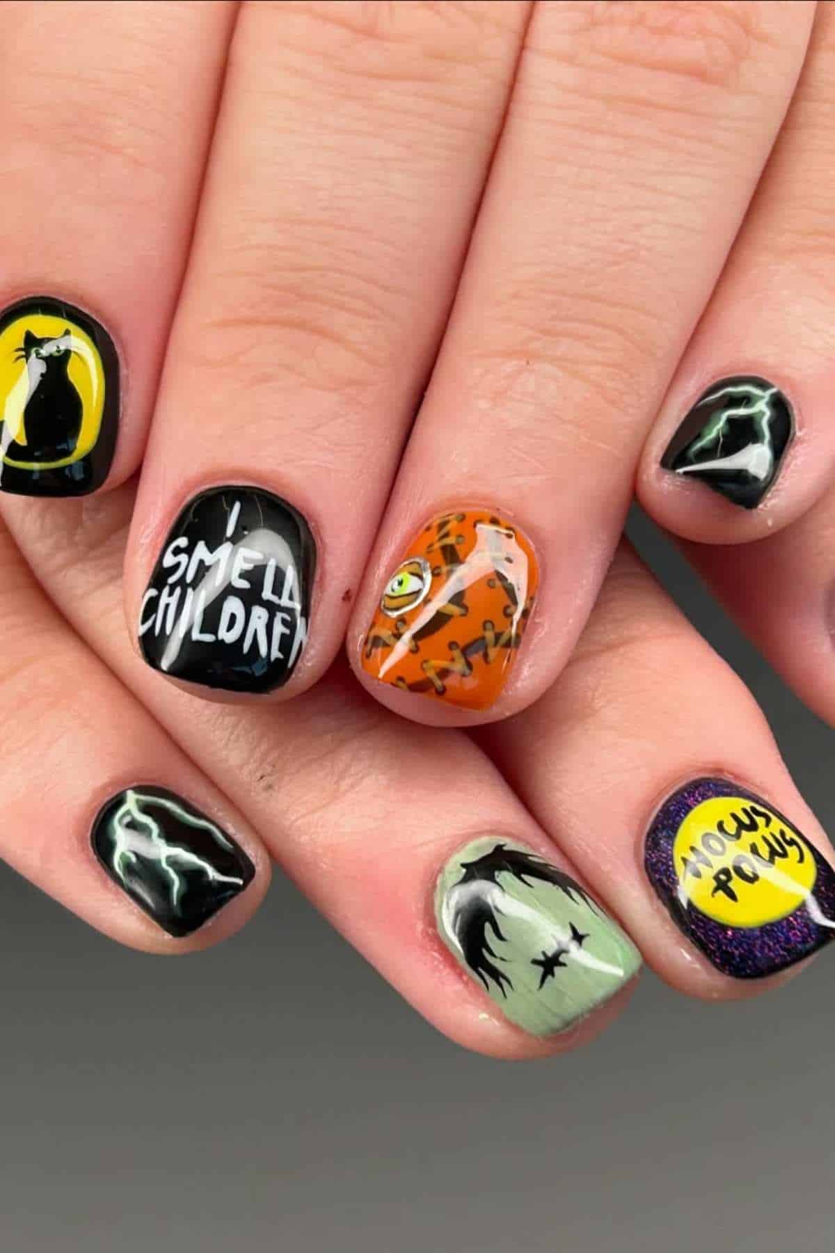 Close-up of a hand with Halloween-themed nail art, featuring witches, lightning, “I smell children,” and “Hocus Pocus” text on different nails.