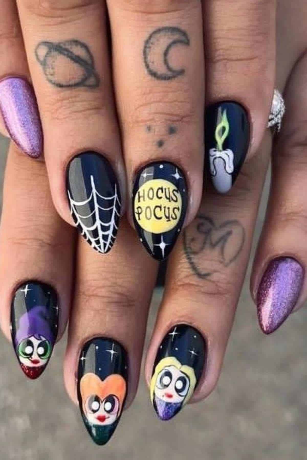 A hand with long nails features Hocus Pocus-themed nail art, including the Sanderson sisters, a spider web, a candle, stars, and a “HOCUS POCUS” design. Fingers have space and letter tattoos.