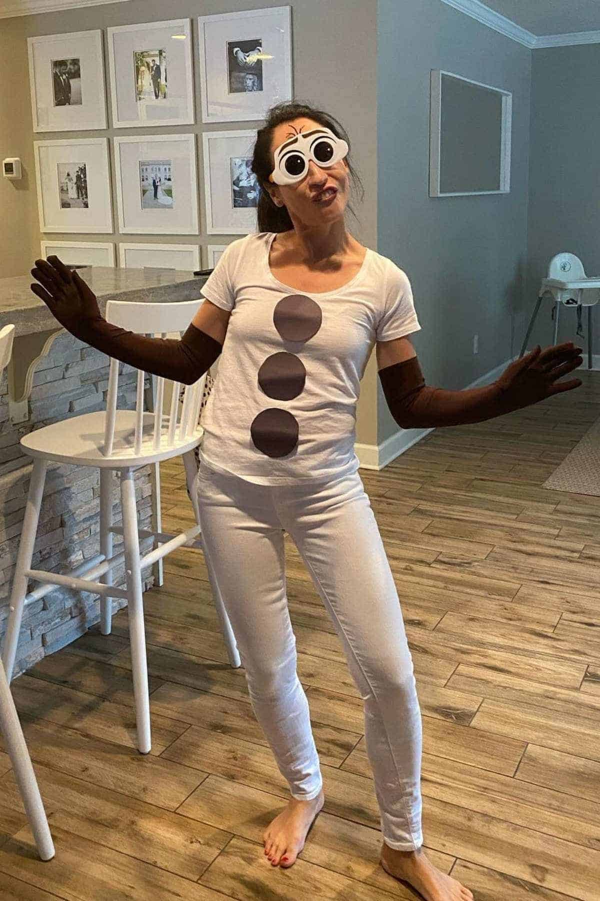 Person wearing a snowman costume made from a white shirt with brown circles, brown gloves, and cartoon eyes, standing barefoot in a living room.