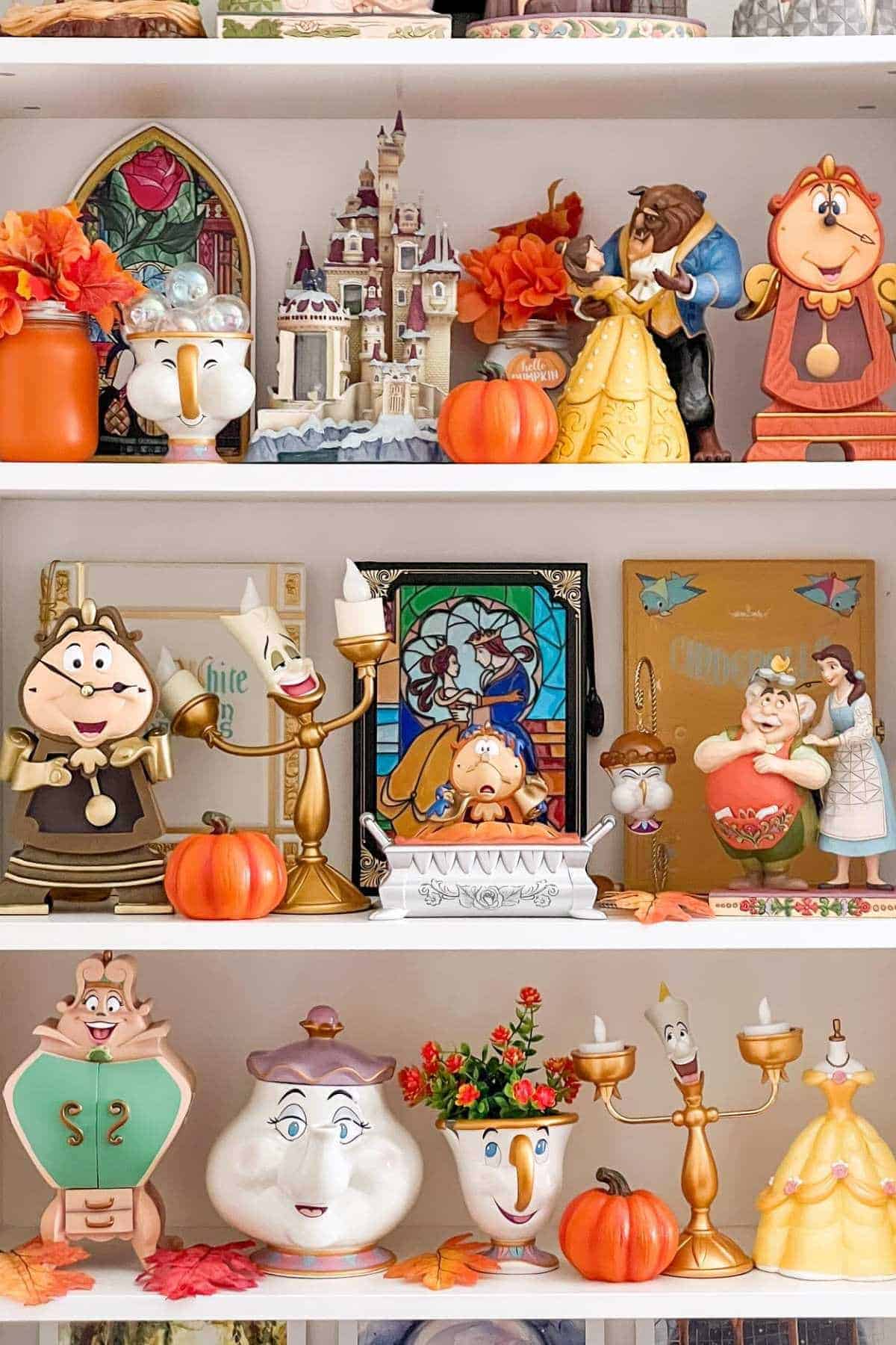 Shelves display Beauty and the Beast figurines, books, stained glass art, faux autumn leaves, and small pumpkins.
