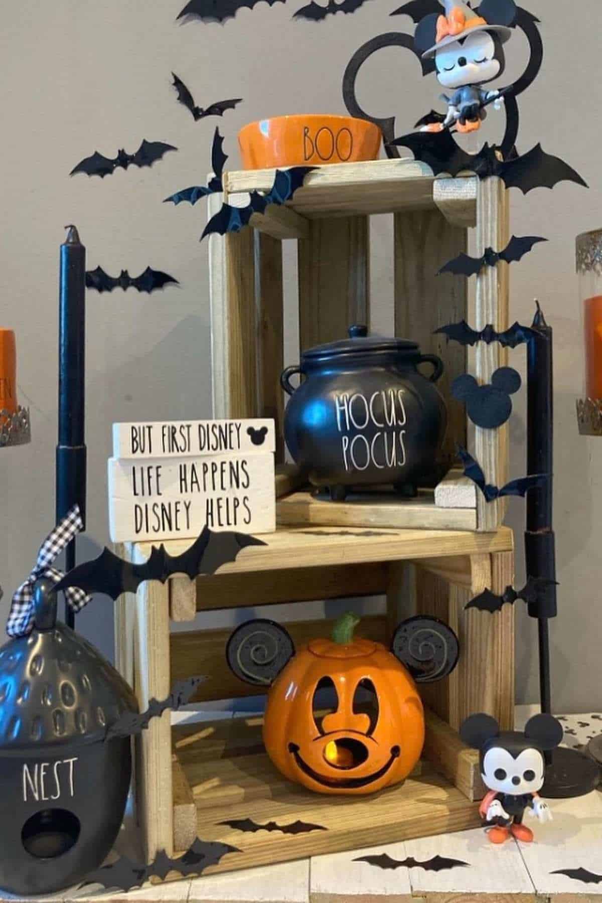 Halloween-themed Disney display with Mickey and Minnie Mouse figures, bat decorations, a “Hocus Pocus” pot, pumpkin with Mickey ears, candles, and a sign that reads “But first Disney.”.