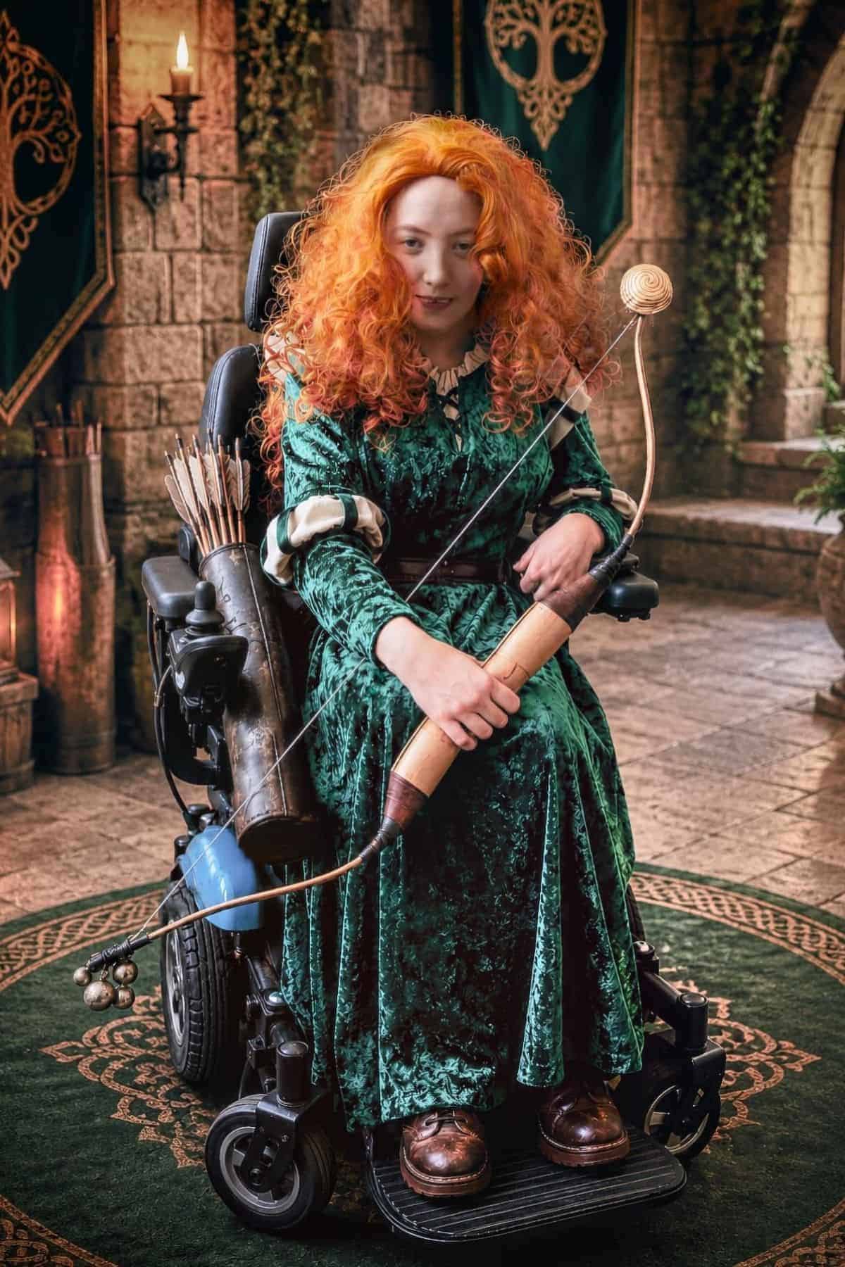 Person with long red curly hair in a green velvet dress sits in a wheelchair, holding a bow and arrows, in a medieval-style stone room with green banners and candlelight.