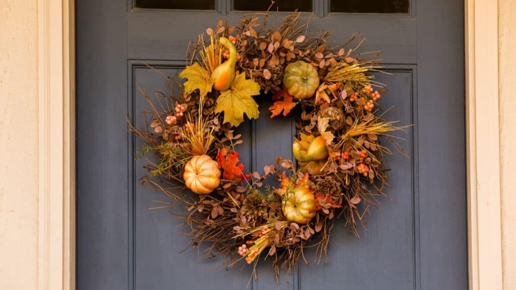 A blue door with a wreath made of twigs, artificial pumpkins, gourds, autumn leaves, and berries, hanging in the center.
