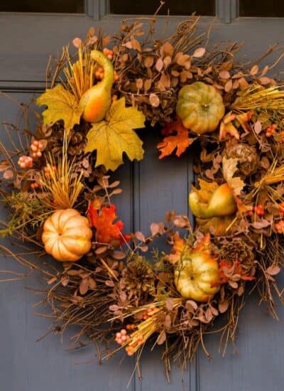 A blue door with a wreath made of twigs, artificial pumpkins, gourds, autumn leaves, and berries, hanging in the center.