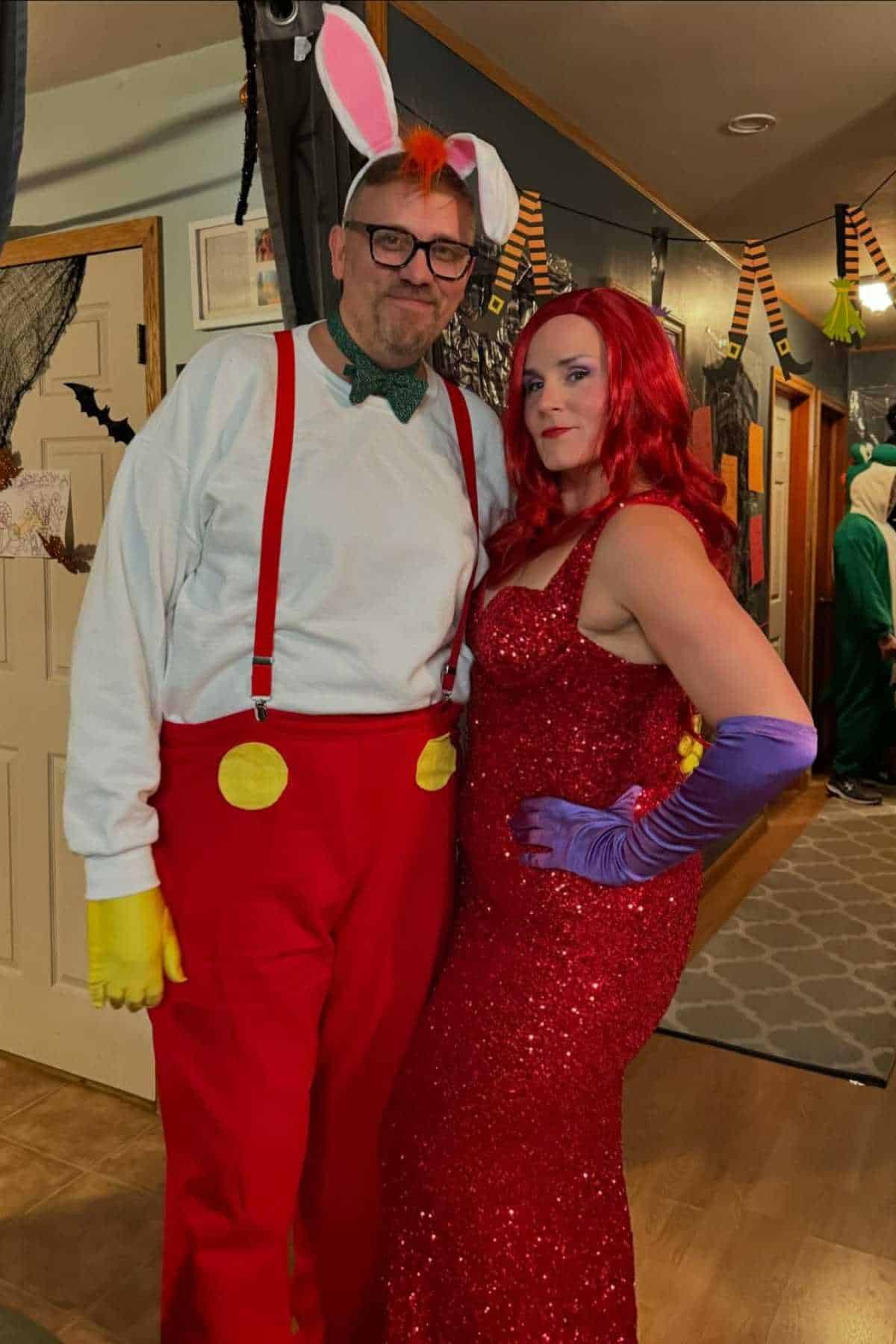 Two adults in costumes: one as Roger Rabbit with bunny ears, red suspenders, and gloves, and one as Jessica Rabbit with a red dress, red wig, and purple gloves, standing indoors at a party.