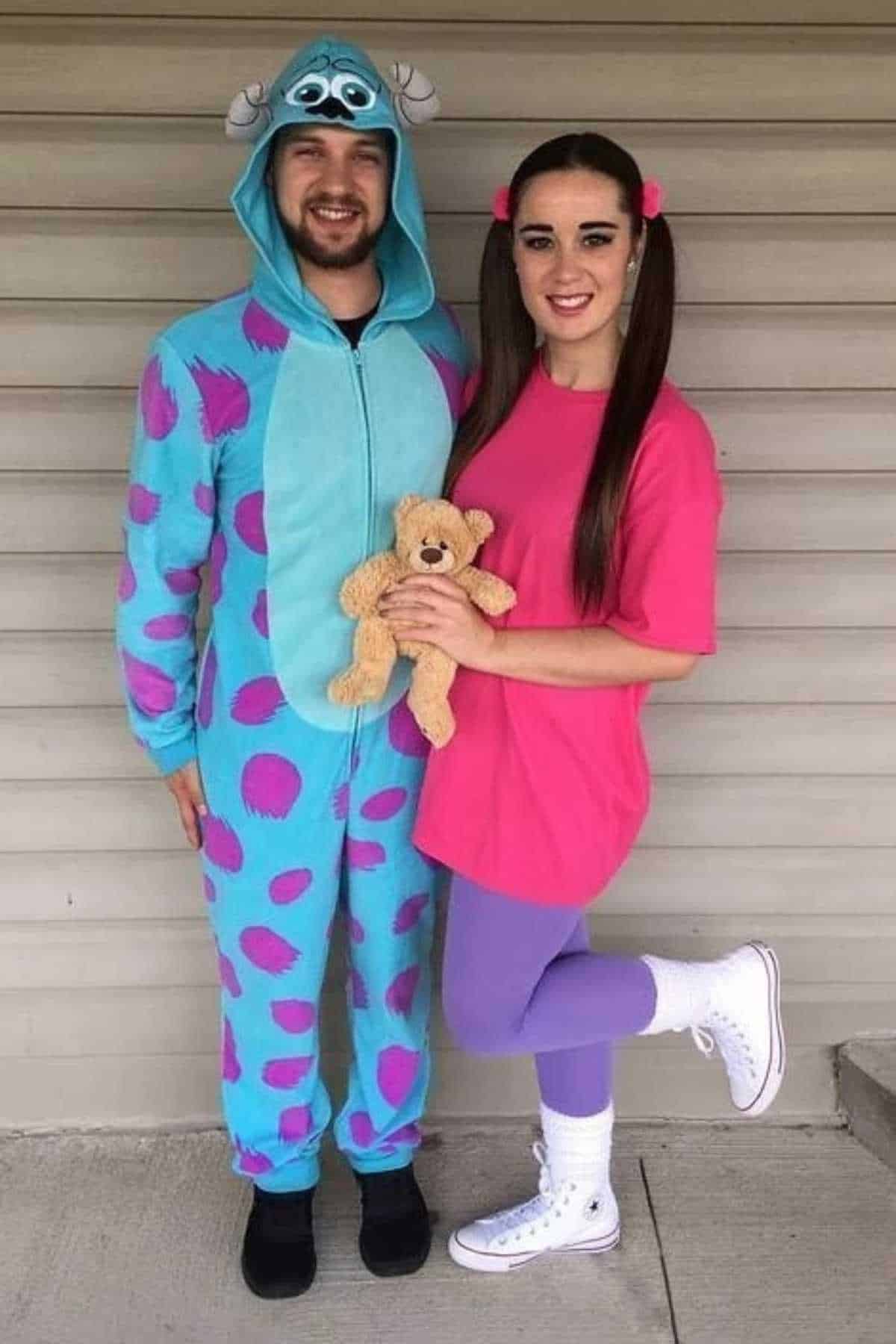 Two people in costumes pose; one wears a blue and purple monster onesie, and the other wears a pink shirt, purple tights, white shoes, and holds a teddy bear.