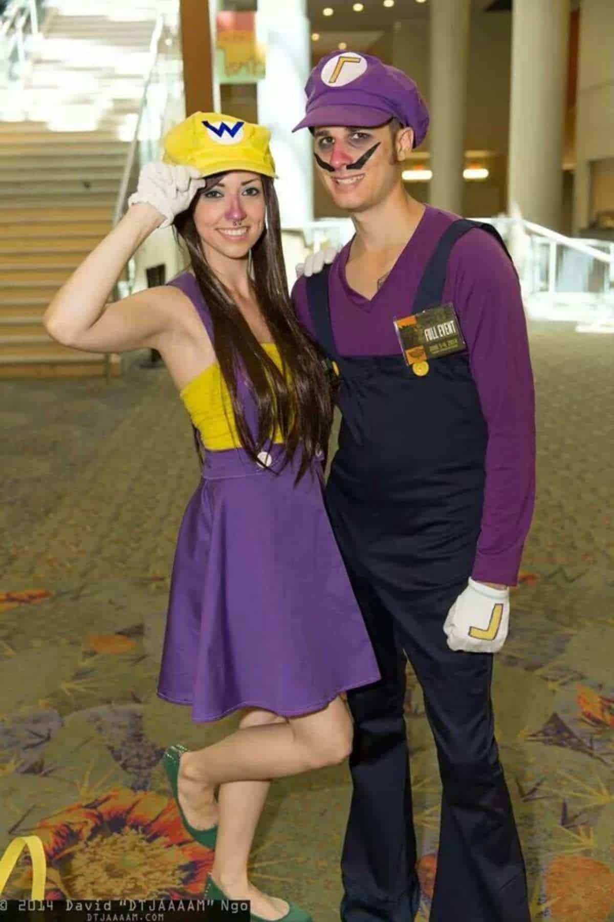 Two people in cosplay outfits pose indoors, dressed as Wario and Waluigi from the Mario franchise, smiling at the camera.