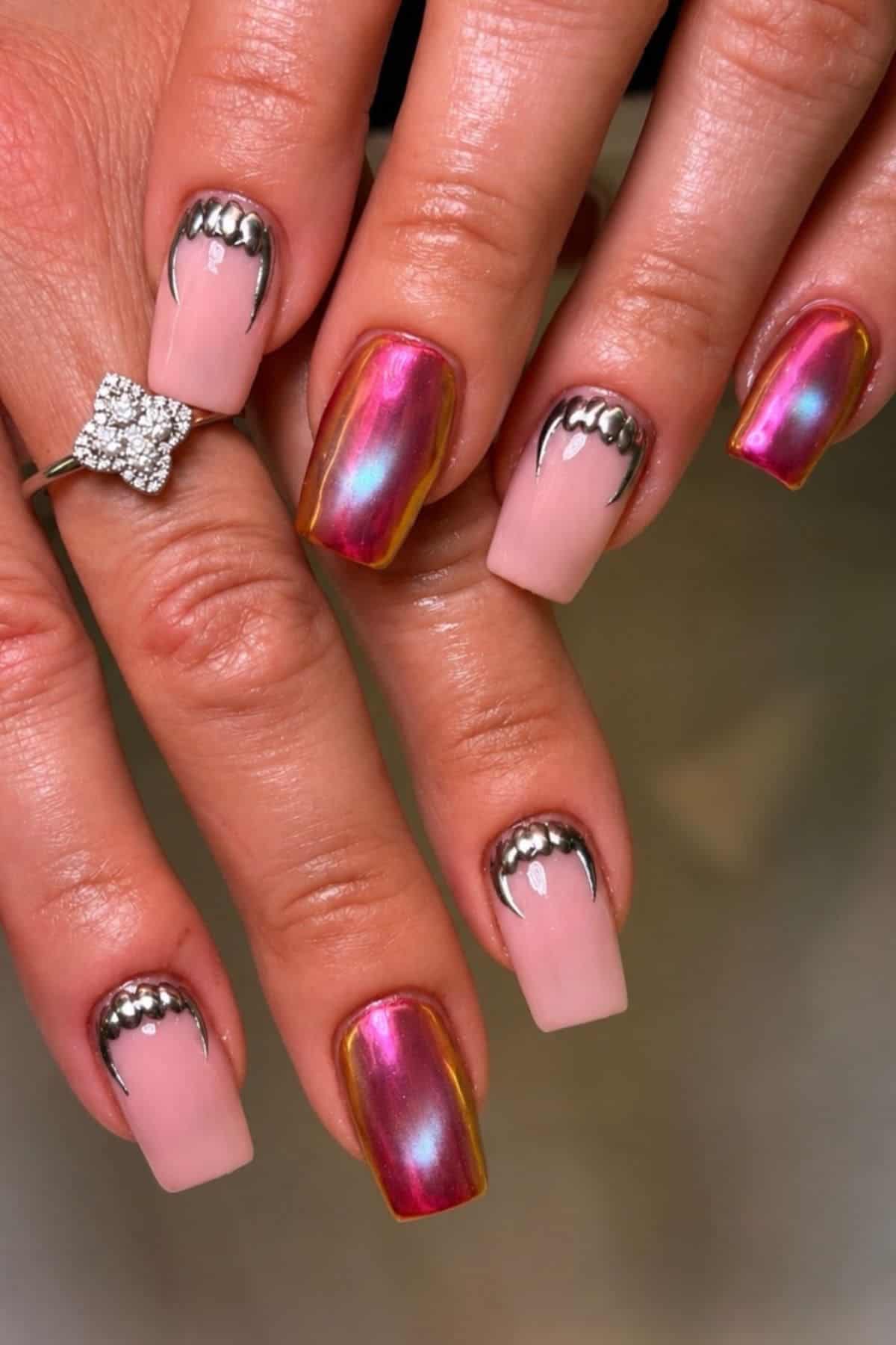 A hand with square-shaped nails featuring pink polish, metallic chrome accents on two middle nails, and silver bead detailing near the cuticles. A diamond ring is on one finger.