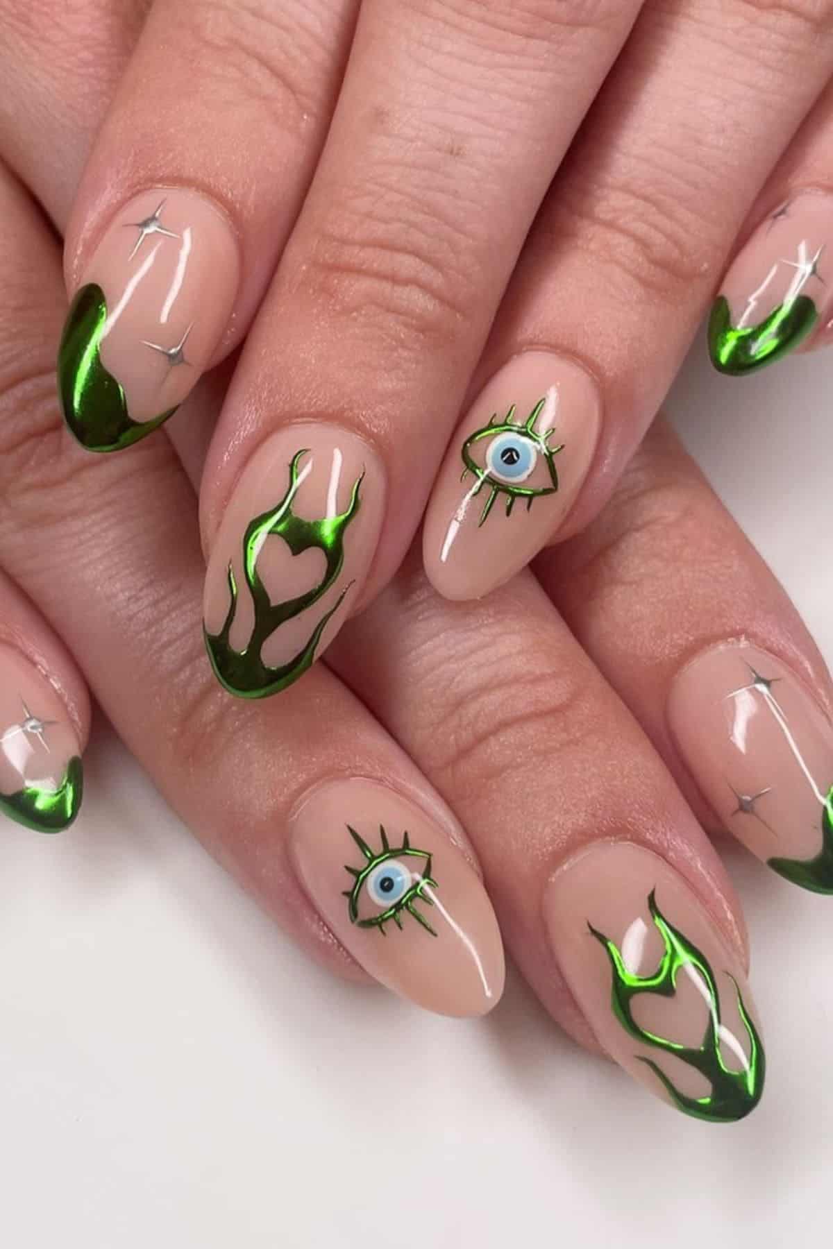 Close-up of manicured nails with green metallic flames, eye designs, hearts, and silver star accents on a nude base.